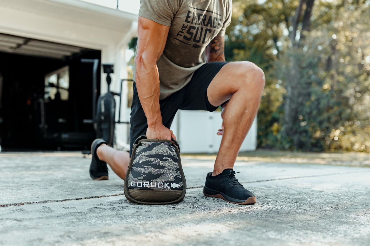 Man exercising outdoors with GORUCK sandbag, wearing athletic gear, rucking workout