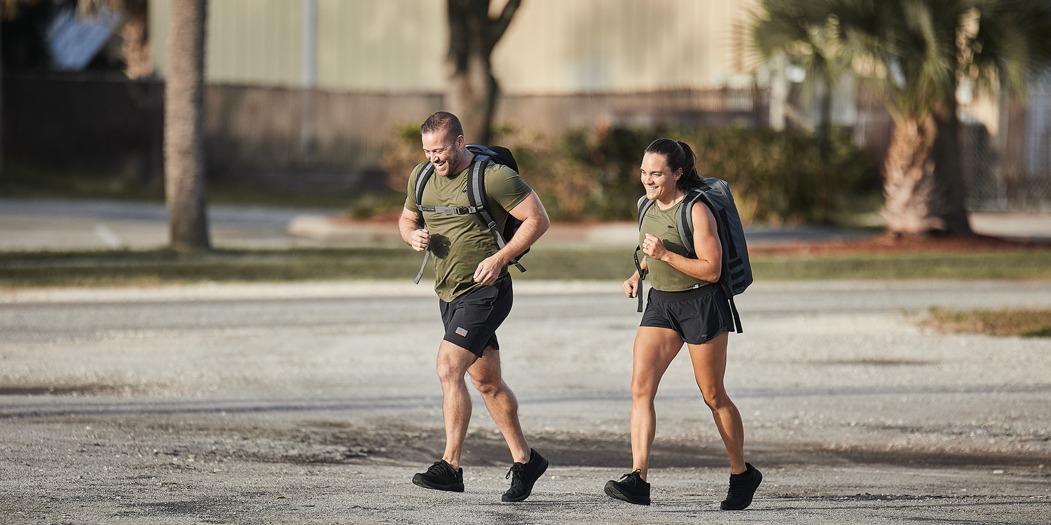 Man and woman jogging outdoors wearing GORUCK gear with backpacks and athletic clothing