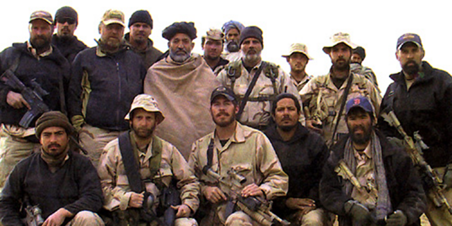 Group of armed soldiers and local men posing together in desert military gear