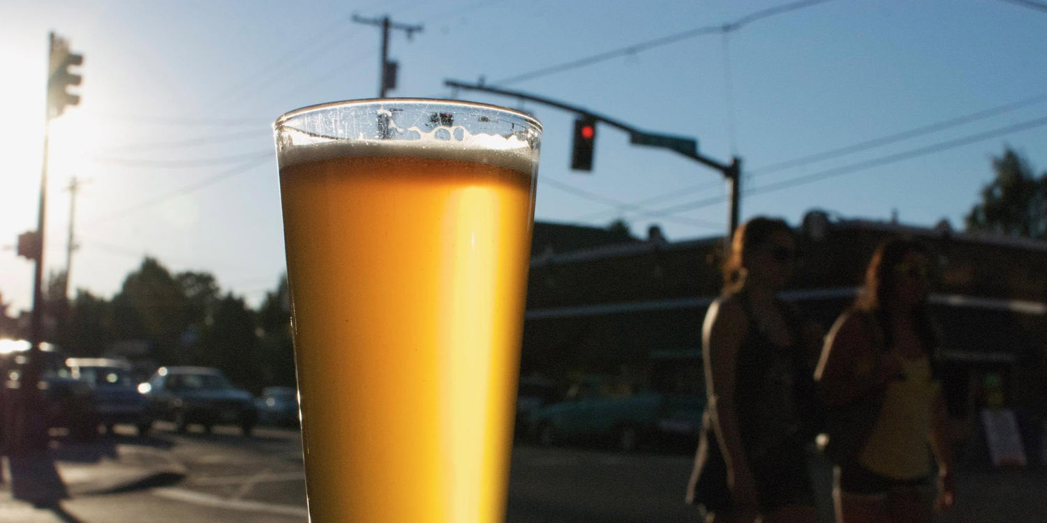 Close-up of a frothy glass of beer with a city street and traffic light in the background