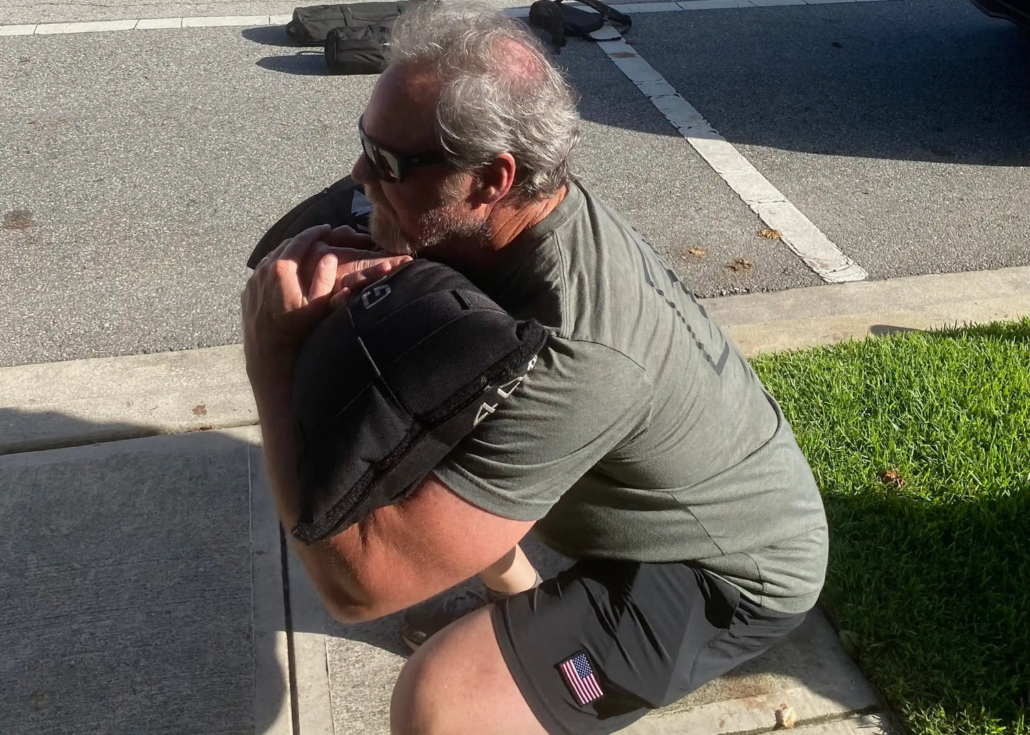 Man outdoors wearing GORUCK gear performing a squat with a weighted sandbag on his shoulders