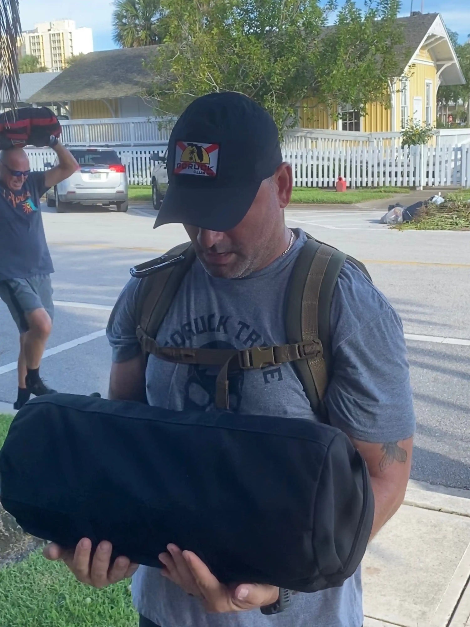 Man wearing GORUCK gear holding a weighted sandbag outdoors during a rucking event