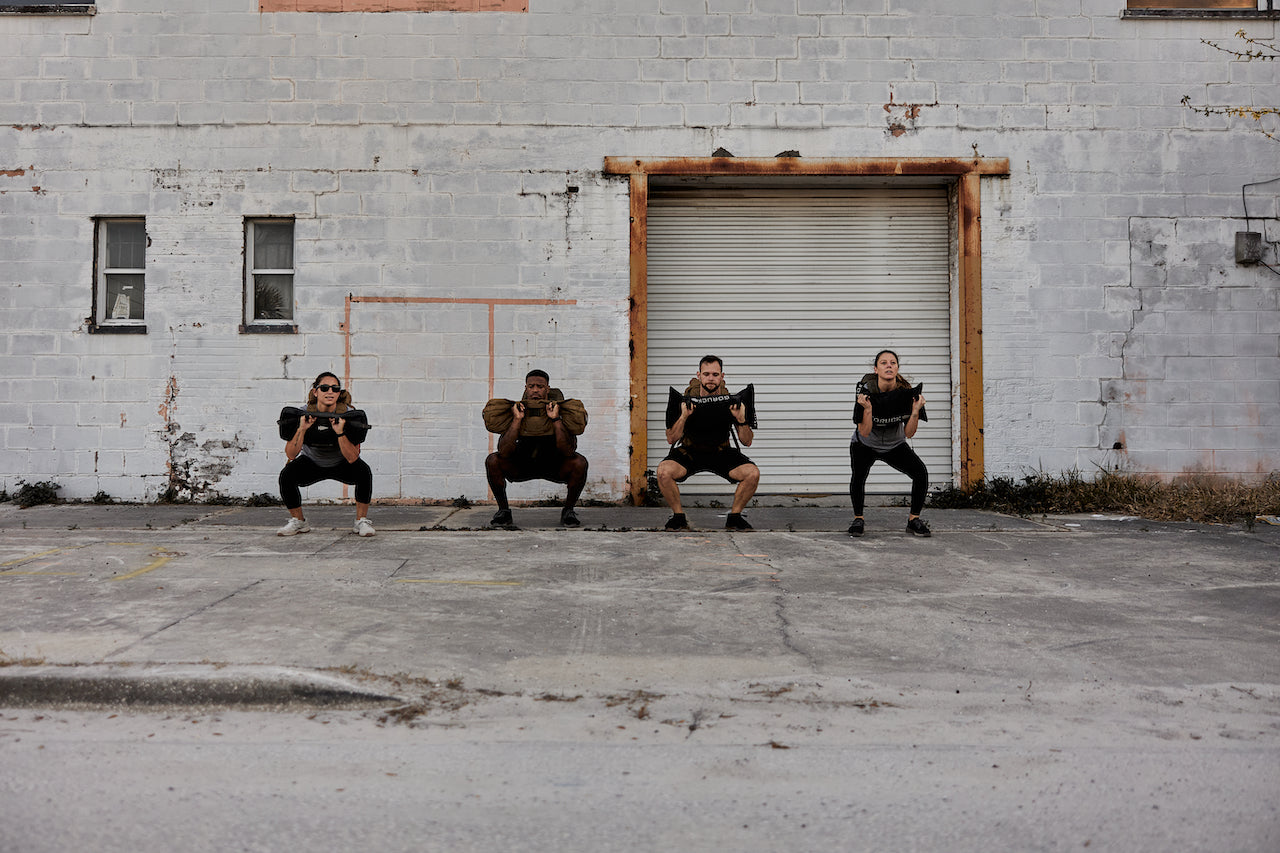 Group rucking workout with GORUCK gear outdoors against an industrial wall