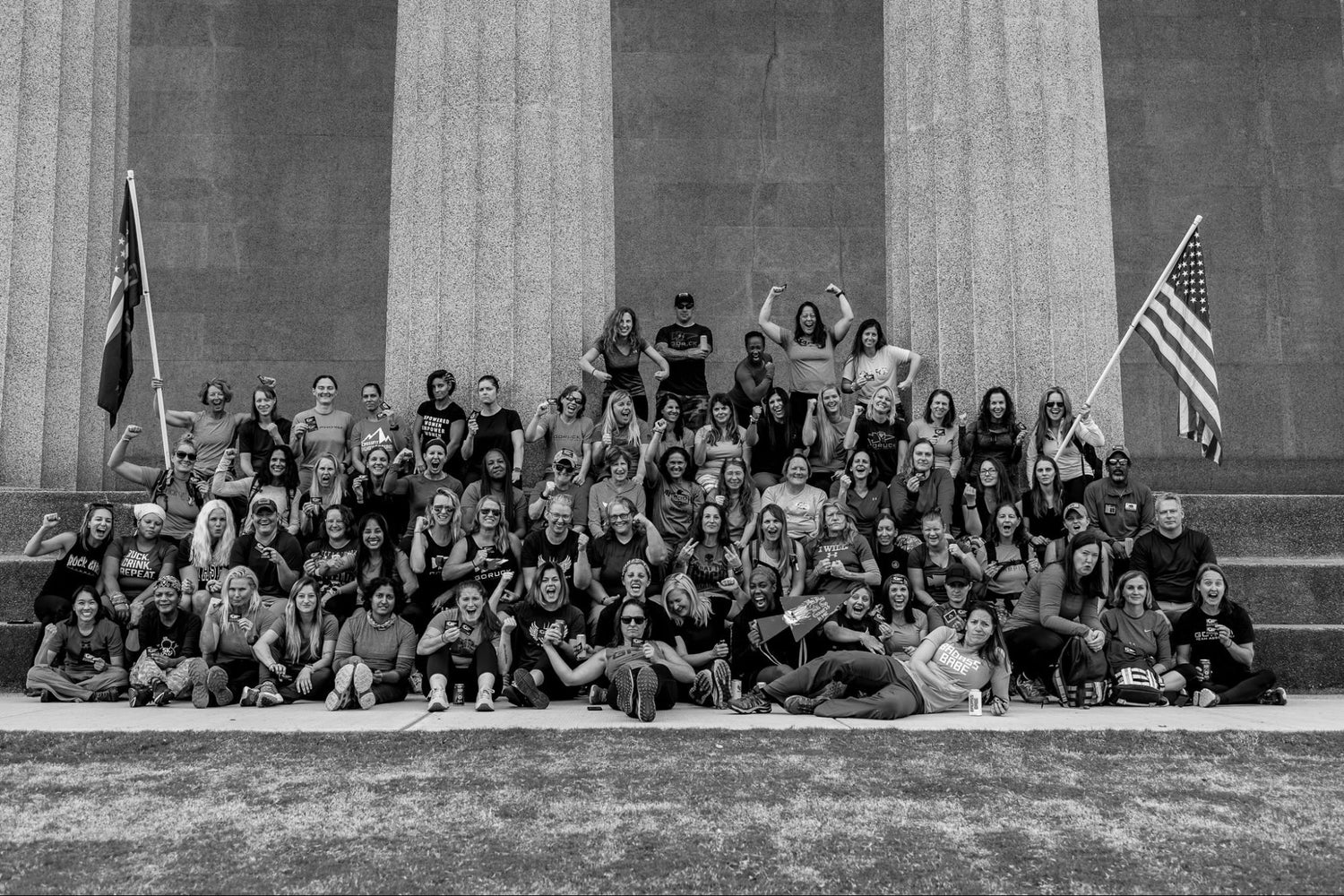 Large group of GORUCK event participants posing on stone steps with American flag, outdoors