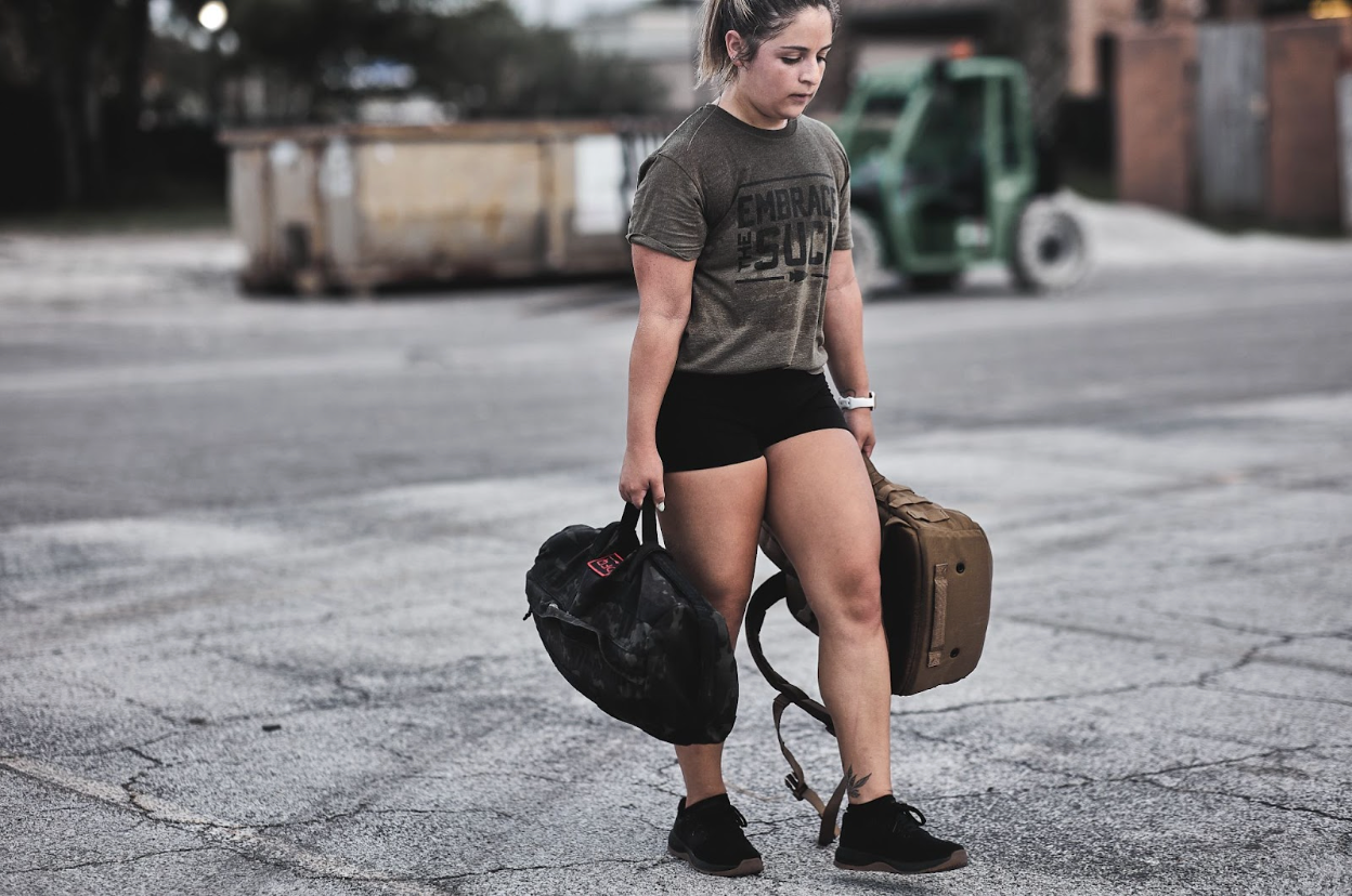 Woman rucking outdoors with GORUCK gear, carrying weighted backpack and sandbag, fitness training