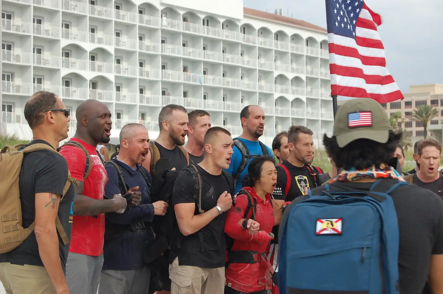 GORUCK group rucking with backpacks and American flag in front of a white hotel building