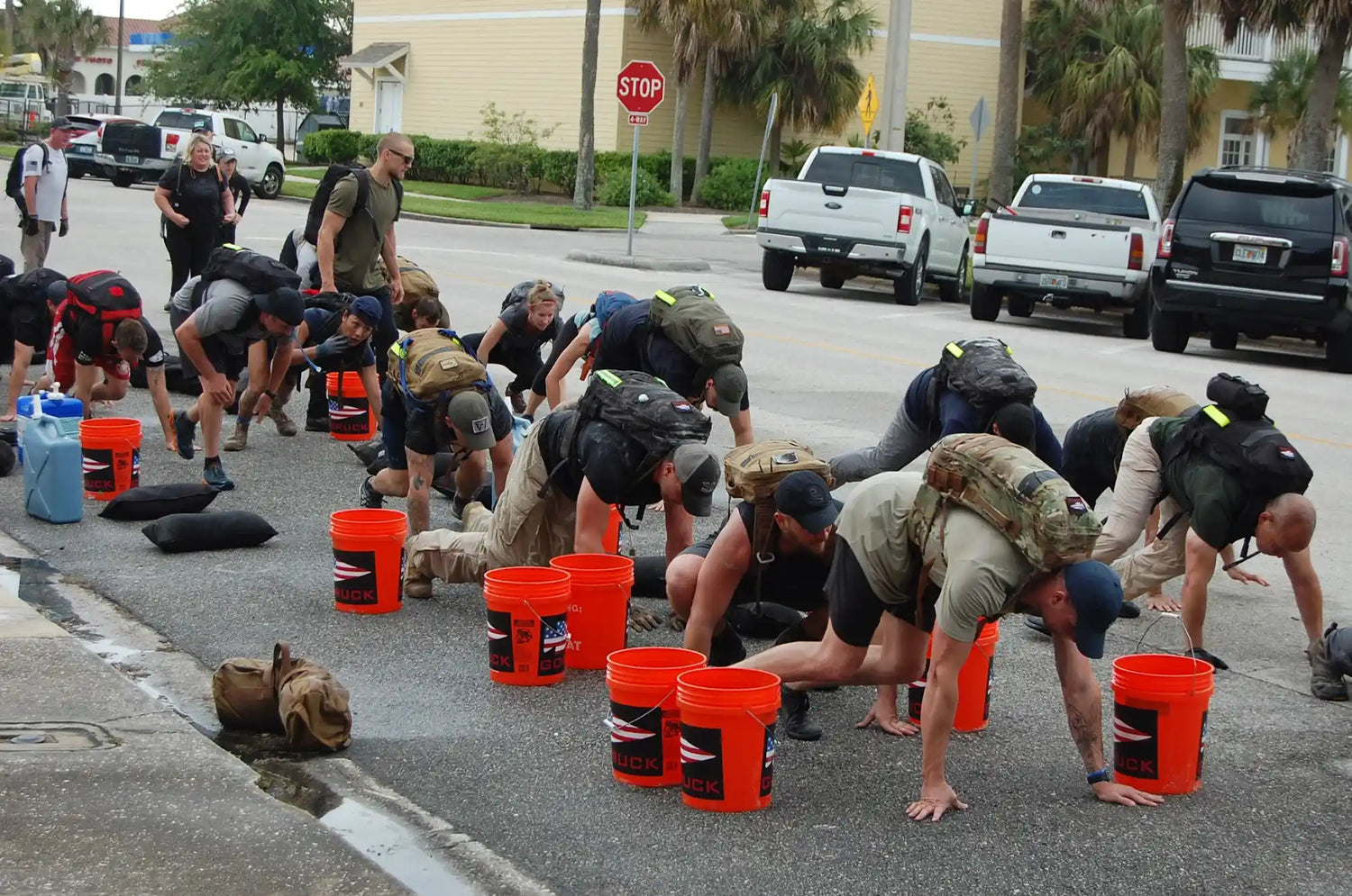 GORUCK event participants with rucksacks doing bear crawls on pavement next to orange buckets