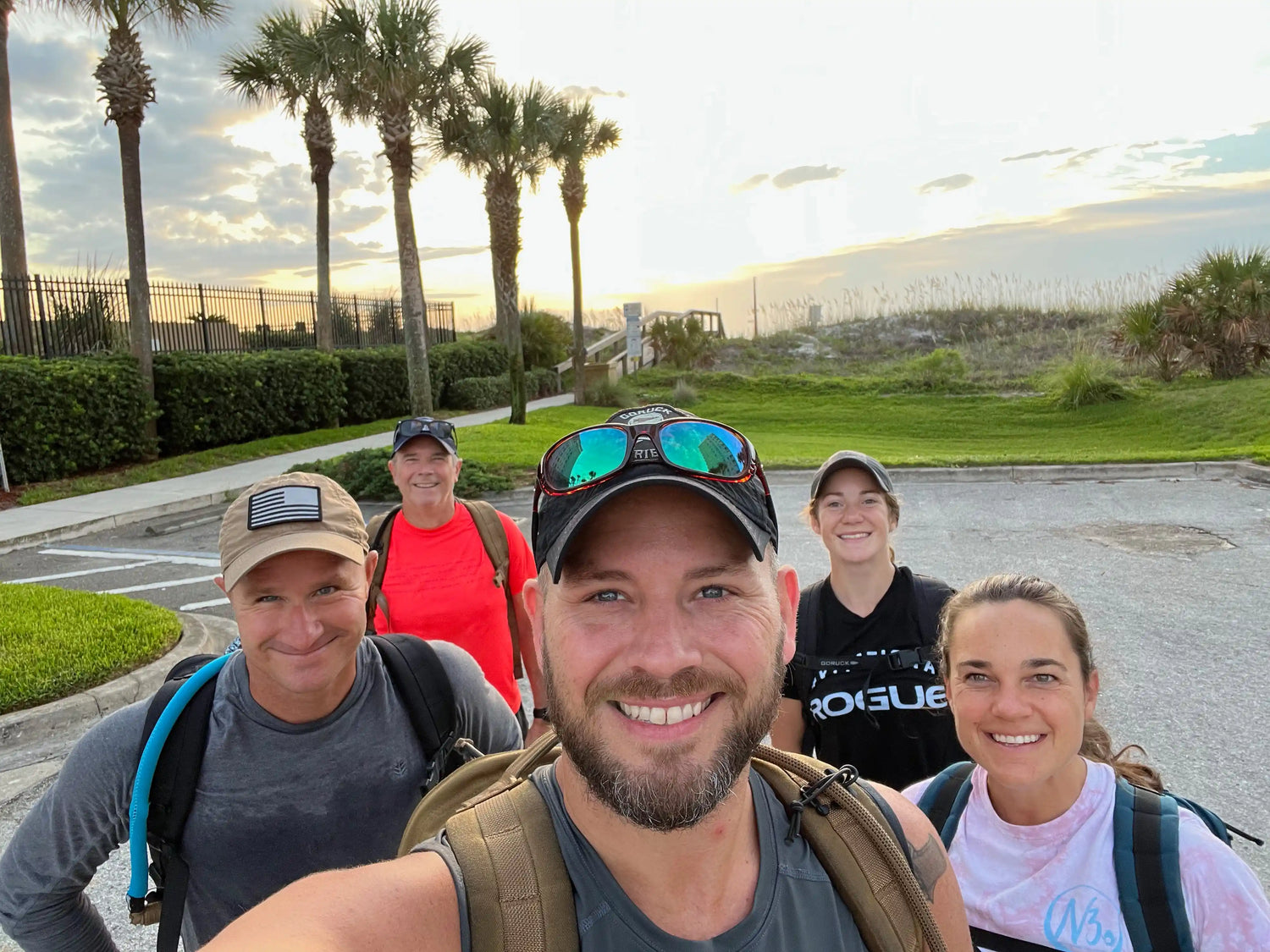 Group of smiling GORUCK ruckers outdoors at sunrise, wearing backpacks and athletic gear