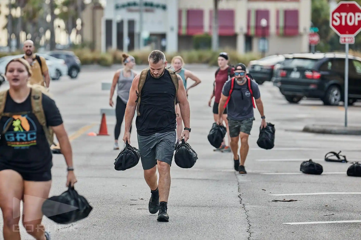 People rucking with weighted bags in a parking lot during a GORUCK training event.