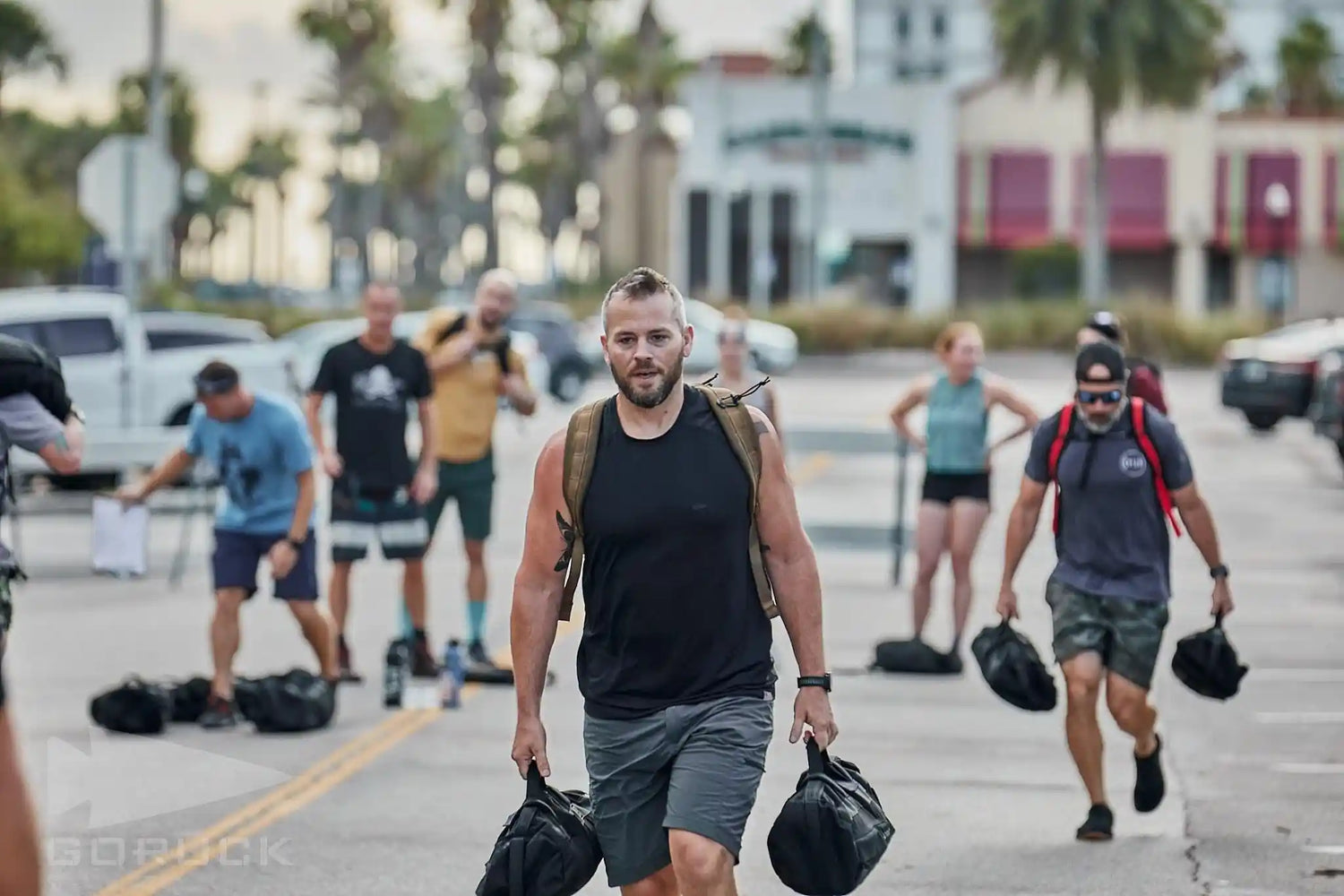 Group rucking event outdoors with participants carrying GORUCK gear and sandbags