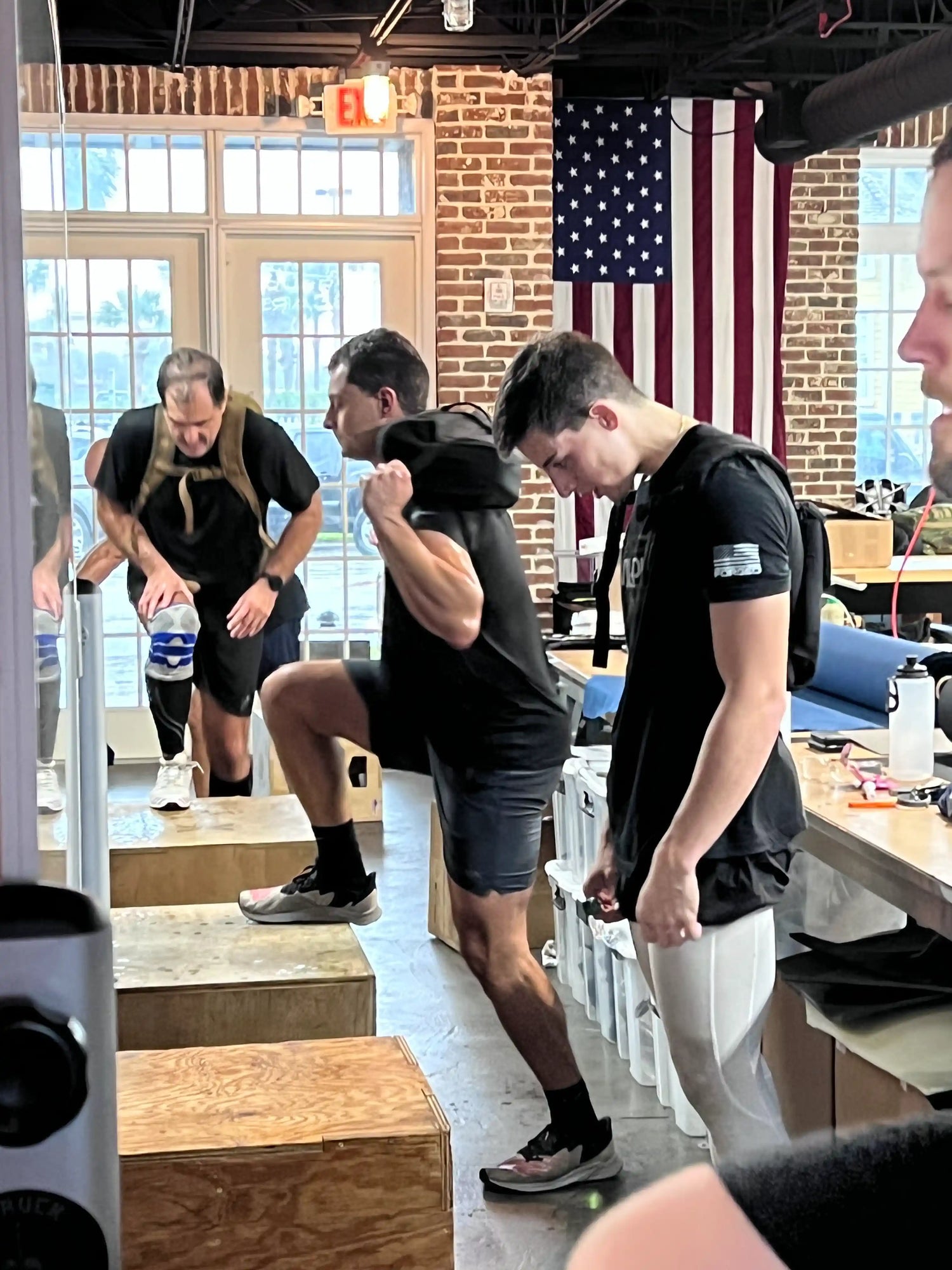 Men training with GORUCK gear indoors, stepping on plyo boxes by American flag