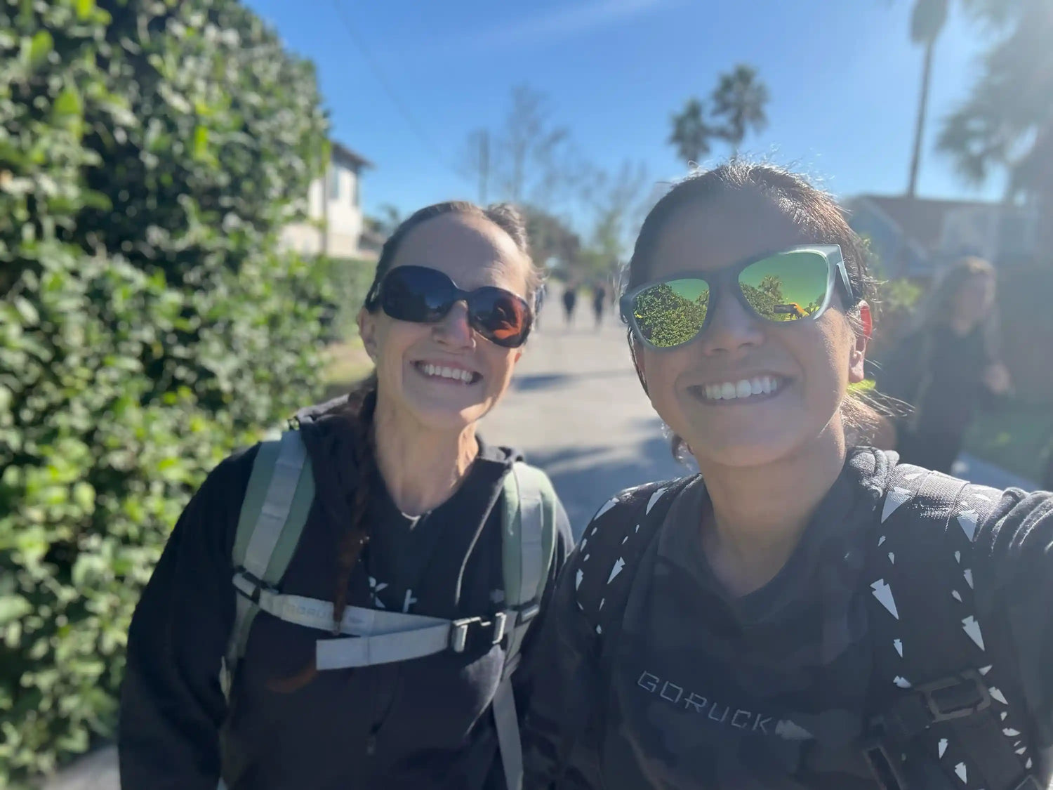 Two women smiling outdoors wearing GORUCK gear and backpacks on a sunny day