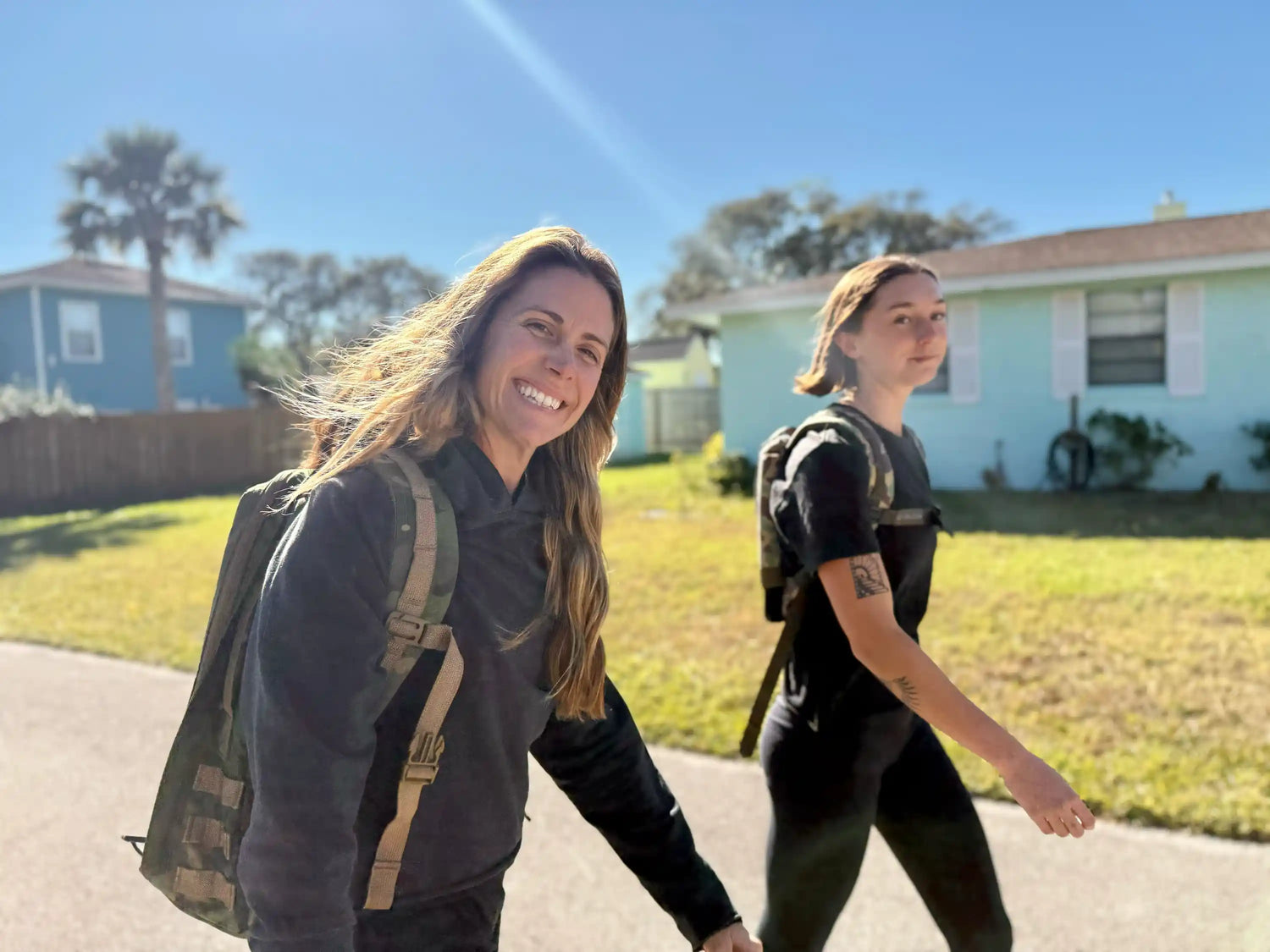 Two women rucking with GORUCK backpacks in a sunny suburban neighborhood