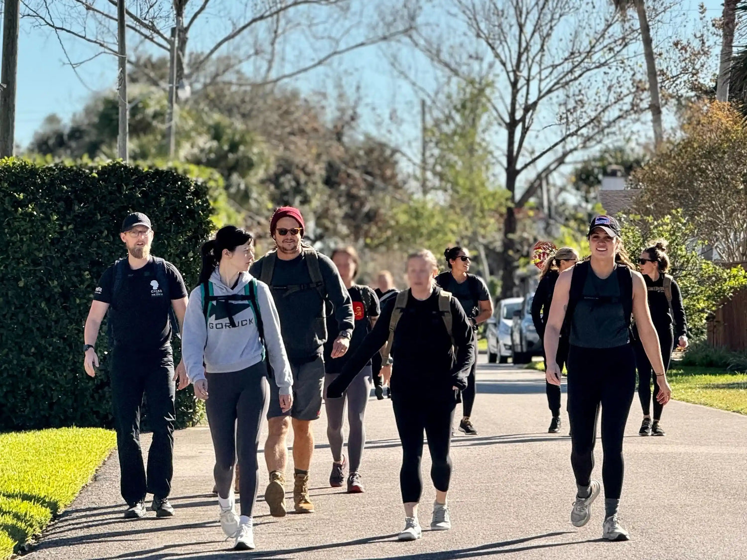 Group of people rucking with GORUCK gear outdoors on a sunny day, walking on suburban street