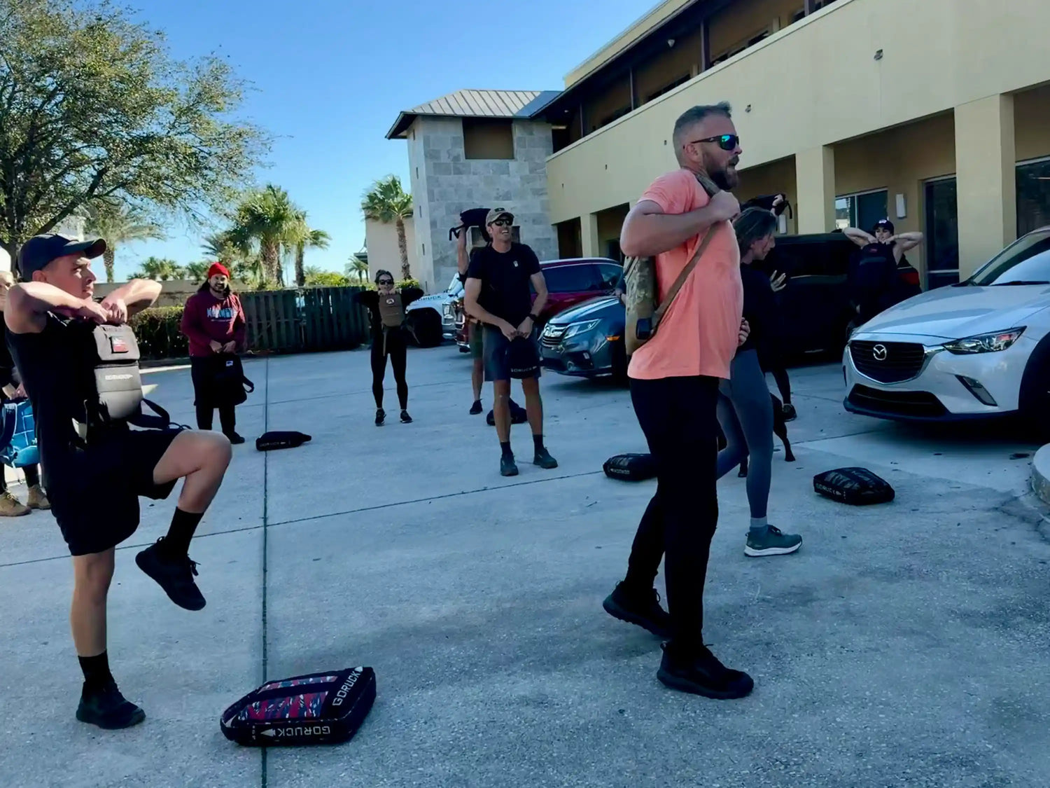 Group doing outdoor rucking workout with GORUCK weighted bags in sunny parking lot