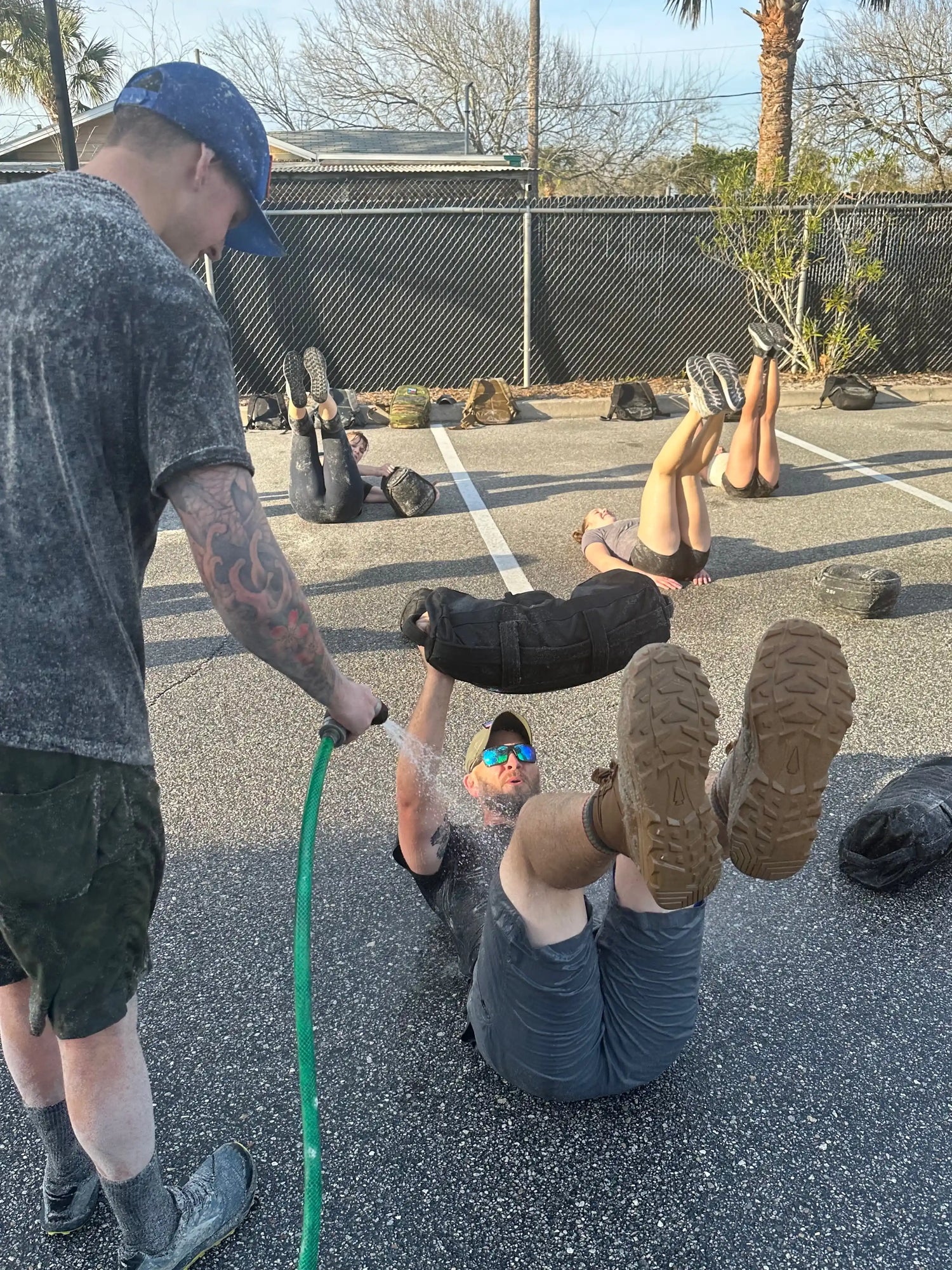 GORUCK outdoor rucking workout, people doing exercises with sandbags, water sprayed, parking lot