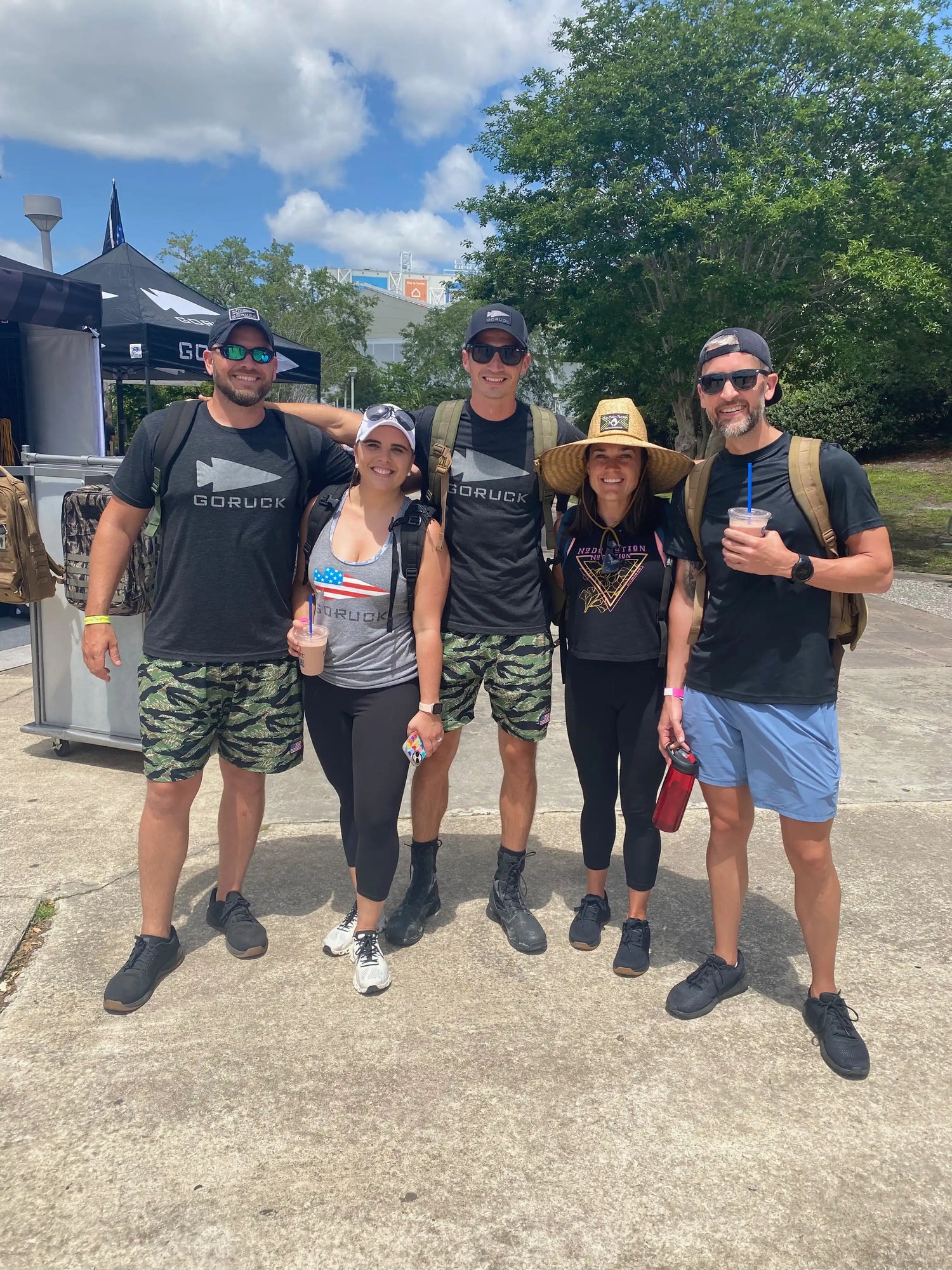 Group of five people outdoors in GORUCK gear, smiling in front of a GORUCK tent on a sunny day