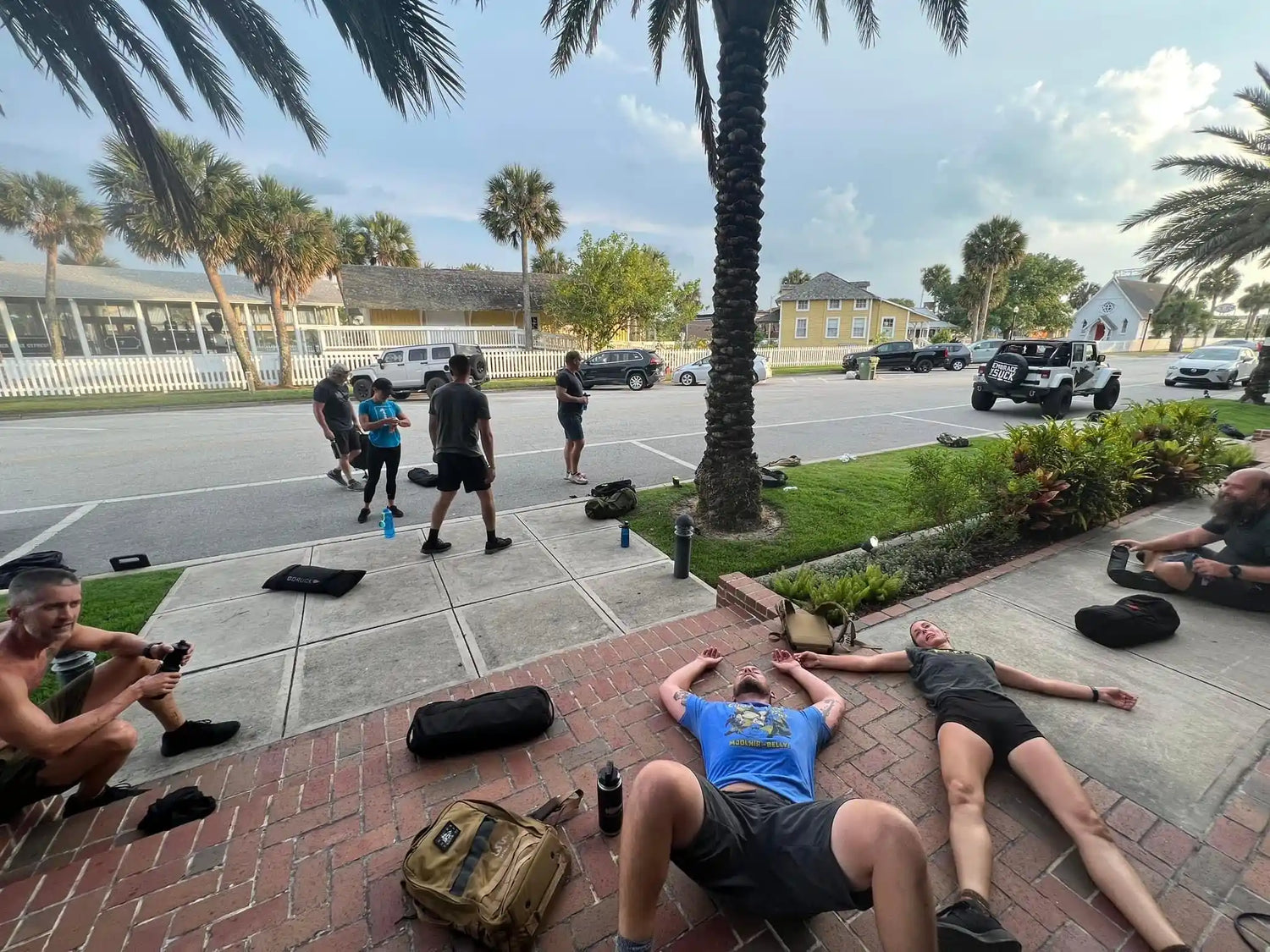 Group of people resting and stretching on brick sidewalk near palm trees in sunny urban area