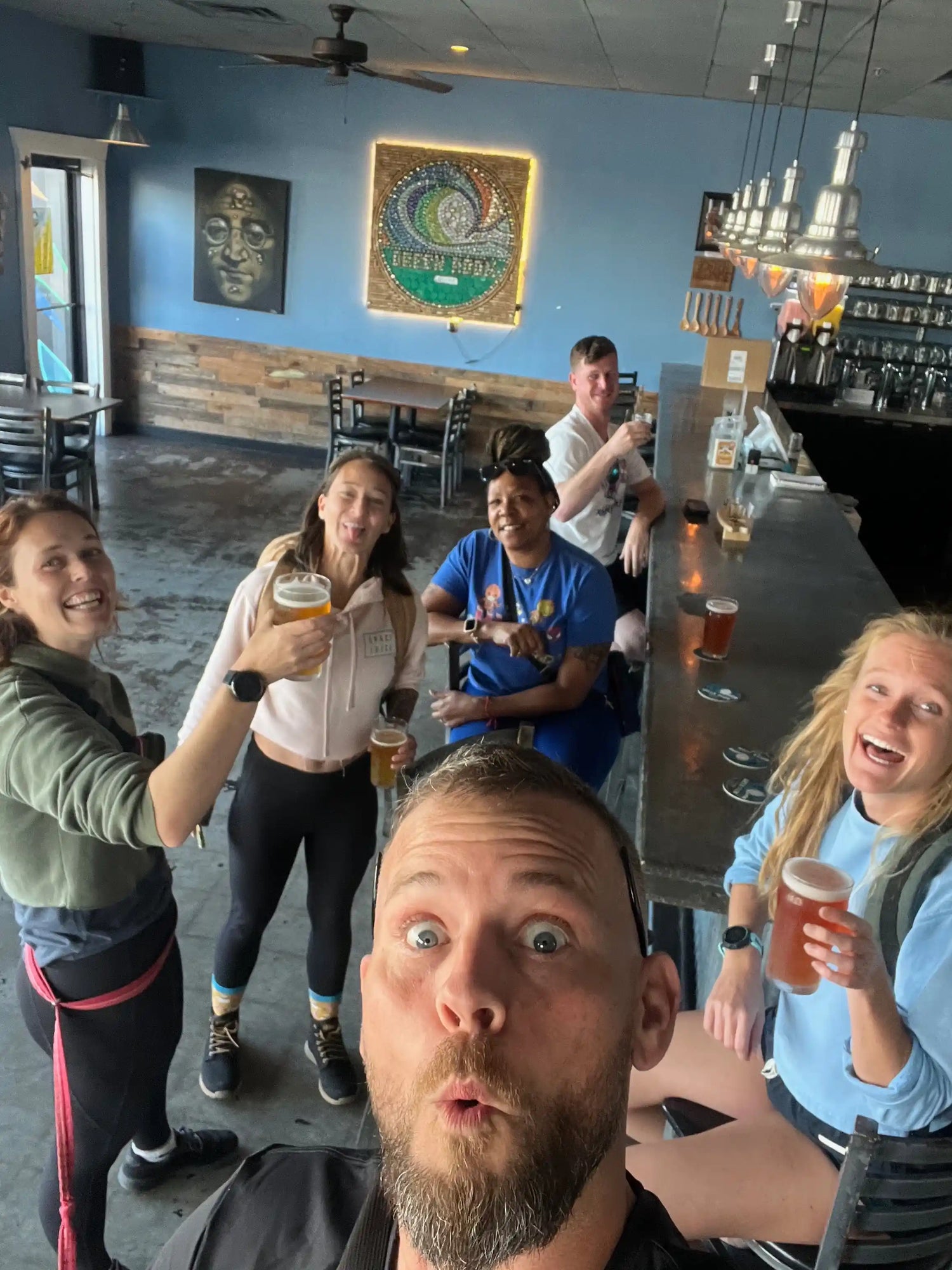 Group of friends in athletic wear celebrating with beers inside a casual bar, GORUCK community vibe