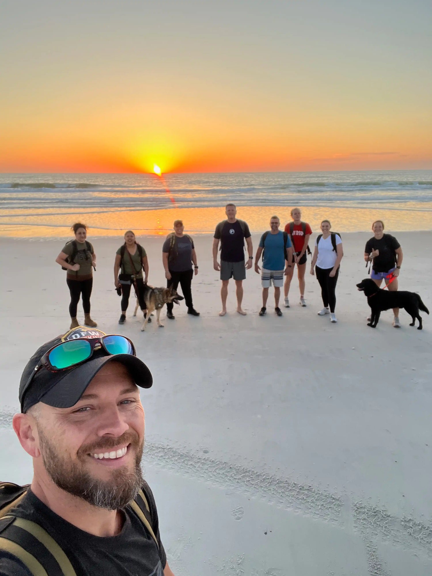GORUCK group rucking with backpacks and dogs on beach at sunrise, community fitness event