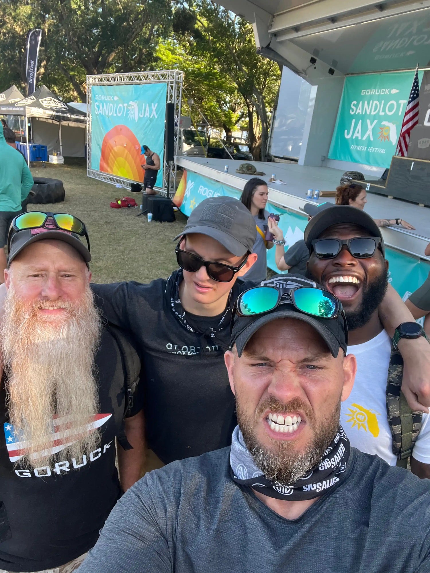 Group of people smiling at GORUCK Sandlot JAX fitness festival outdoors, event stage in background
