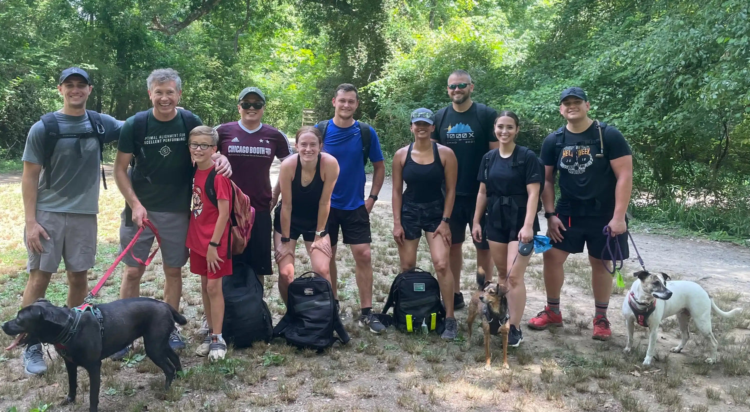 Group of people with dogs rucking outdoors, wearing GORUCK gear in a wooded park setting