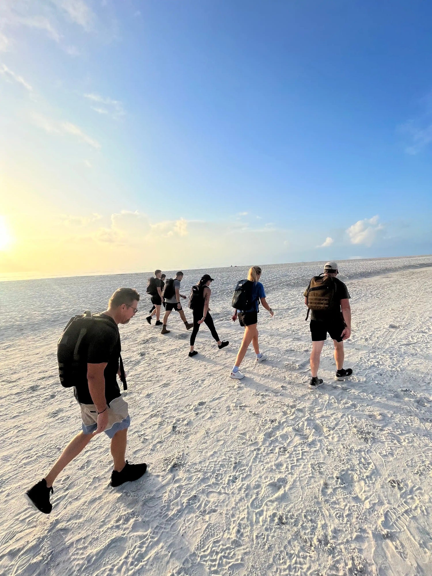 Group of people rucking on a sandy beach at sunrise wearing GORUCK backpacks
