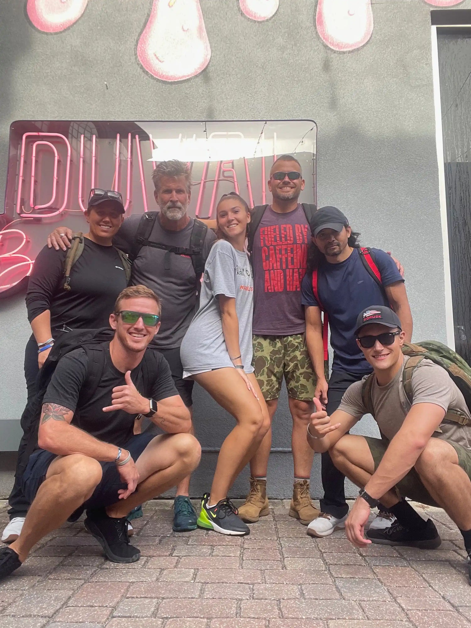 Group of people in athletic gear with GORUCK backpacks posing outside under neon Duval sign