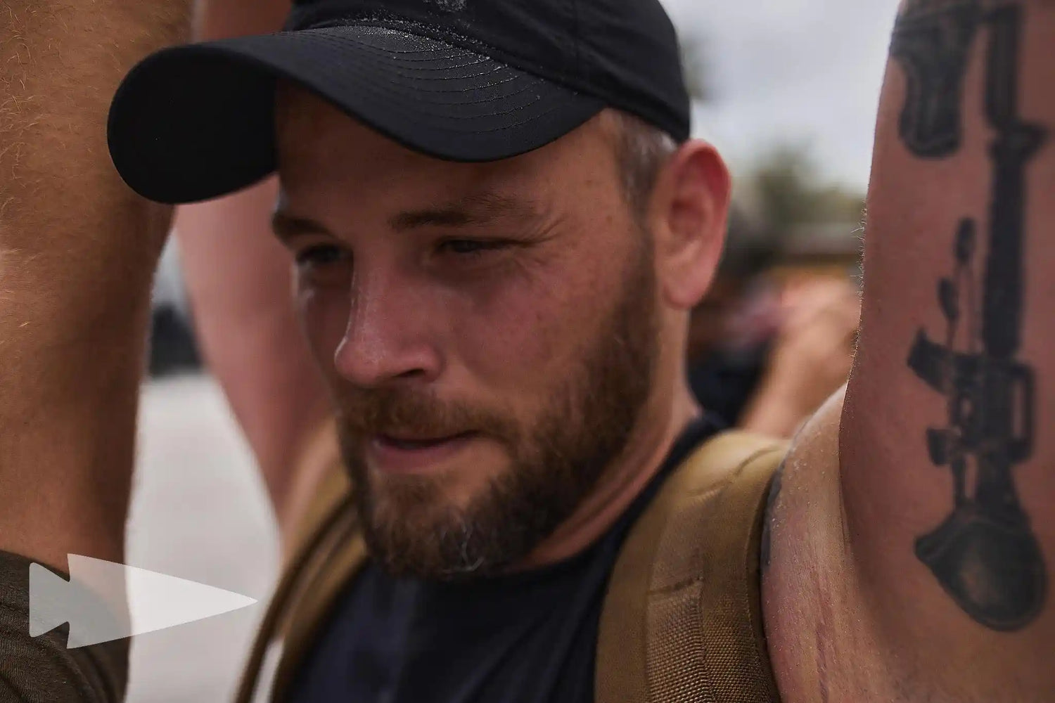 Man in GORUCK gear and black cap, close-up, outdoors, showing tattooed arm.