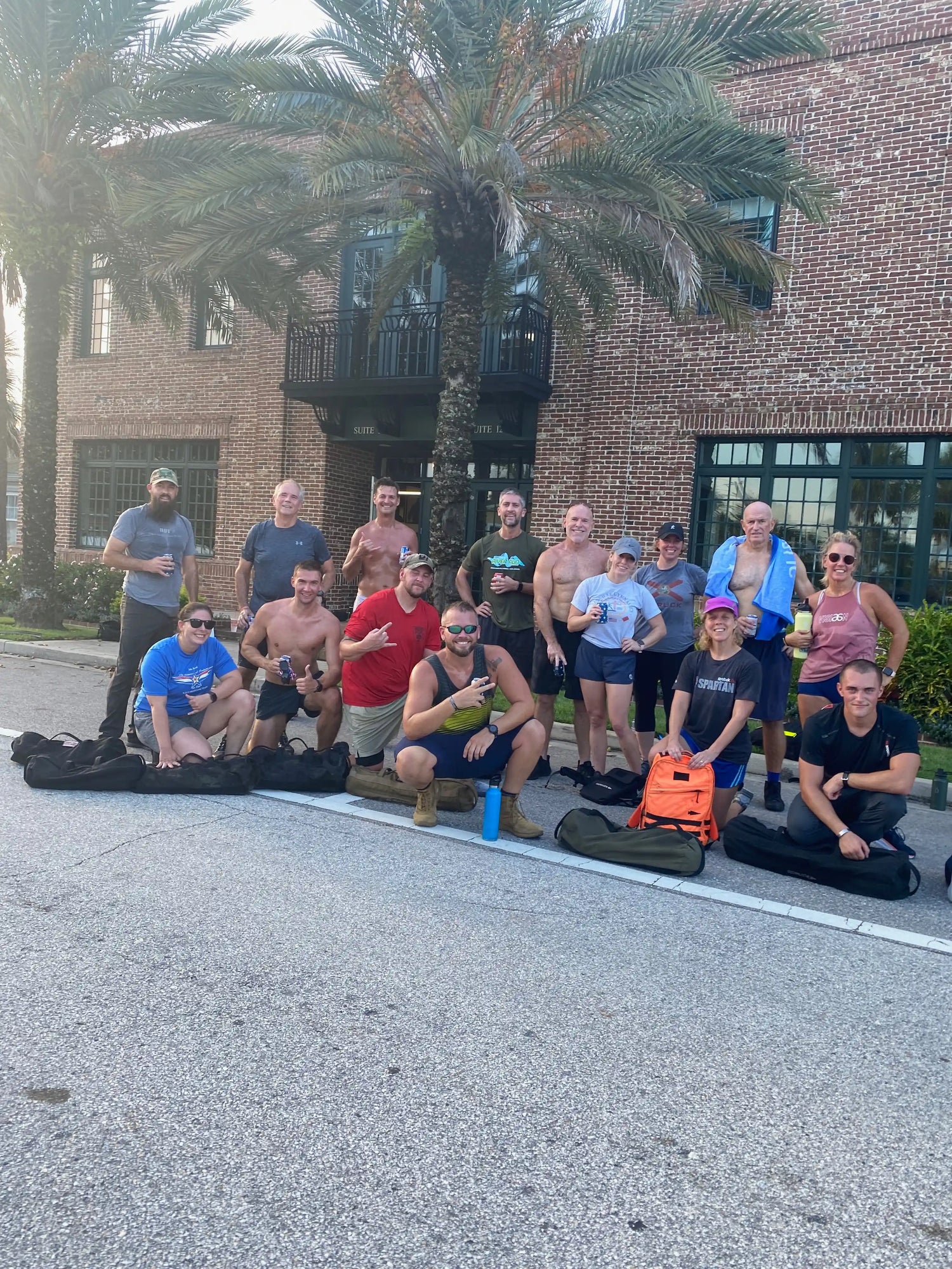 GORUCK group outdoors with rucksacks in front of brick building and palm trees