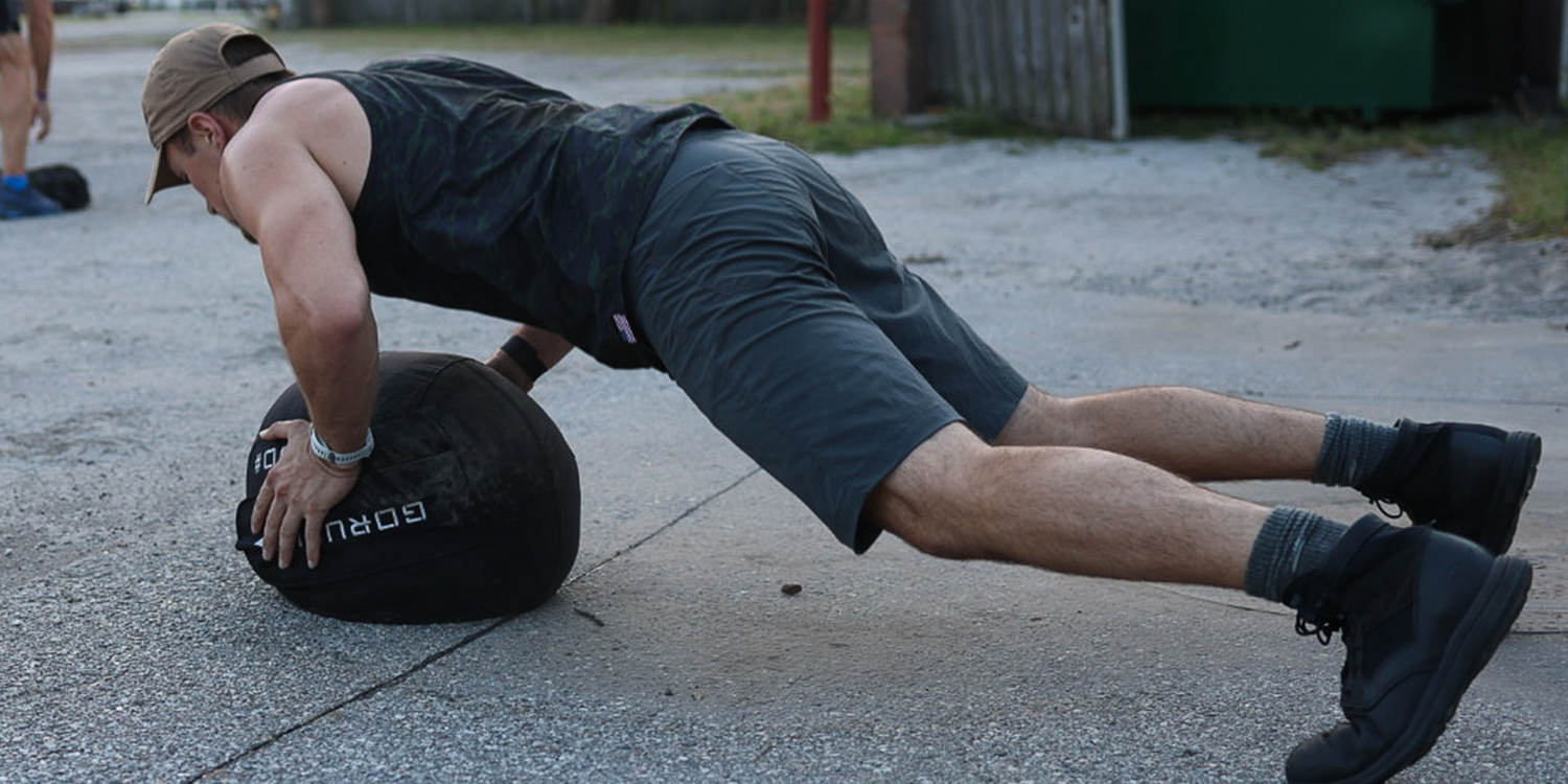 Man doing outdoor push-ups on a GORUCK medicine ball, wearing athletic gear