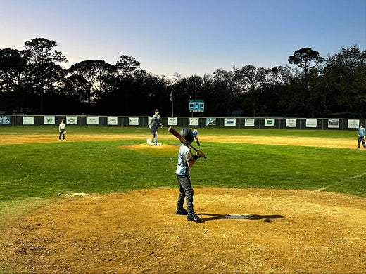 Youth baseball game at dusk with batter at home plate and pitcher on mound in green field