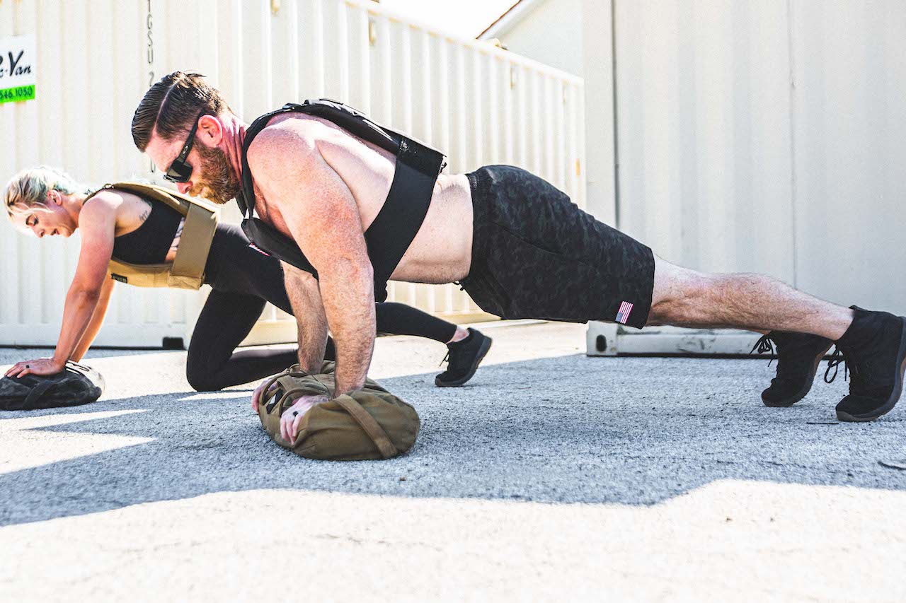 Two people wearing weighted vests do planks outdoors with GORUCK rucking gear