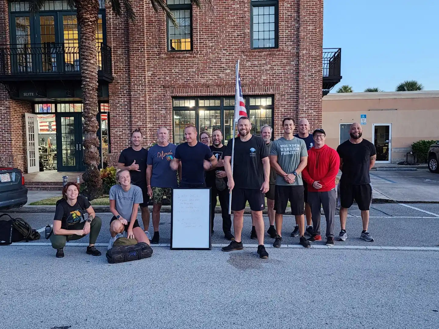 GORUCK group outside brick building with American flag, rucksacks, and whiteboard