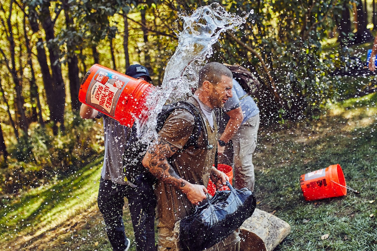GORUCK outdoor rucking event, man with weighted backpack gets splashed with water, teamwork challenge