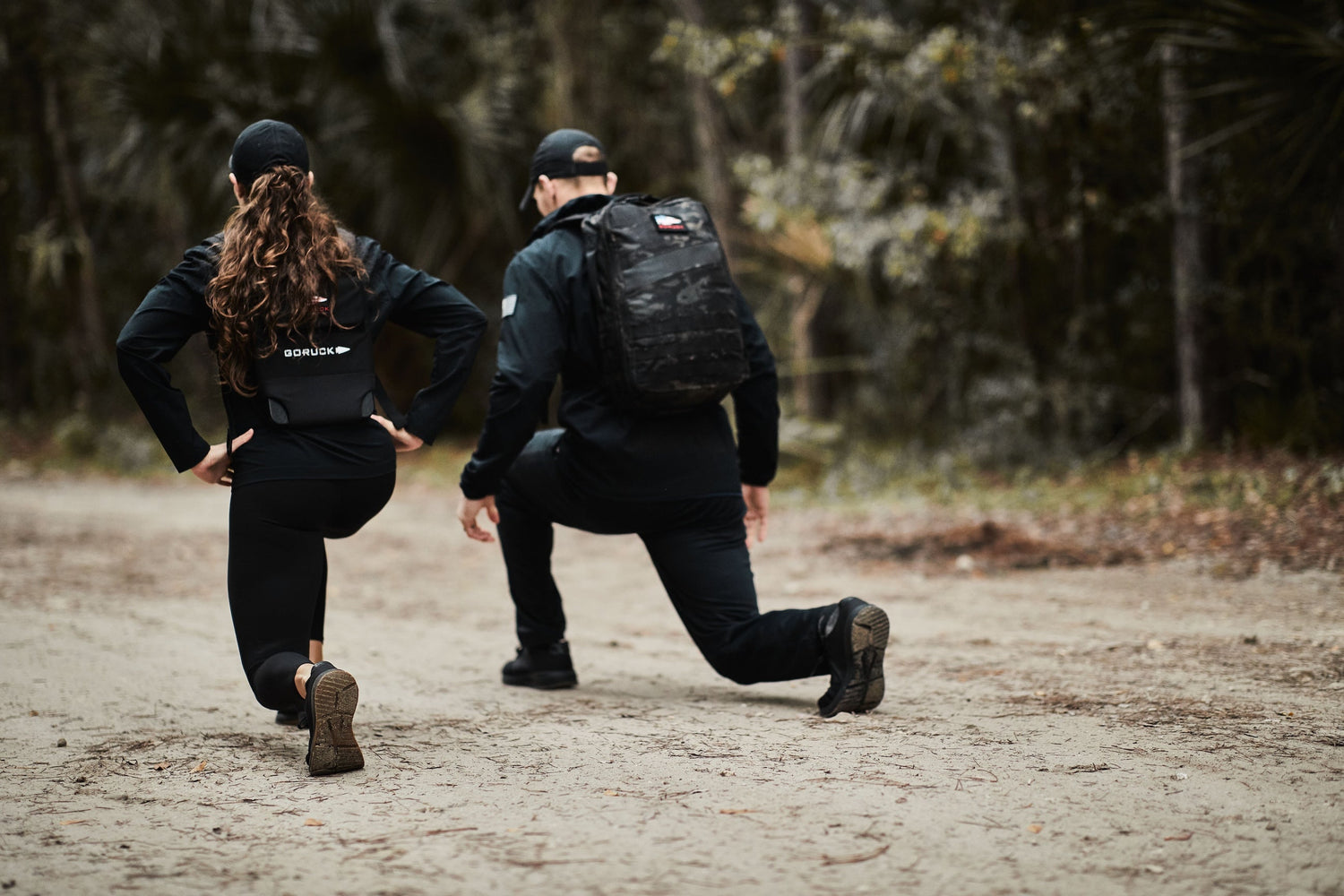 Two people rucking with GORUCK gear, doing lunges on a forest trail, outdoor fitness