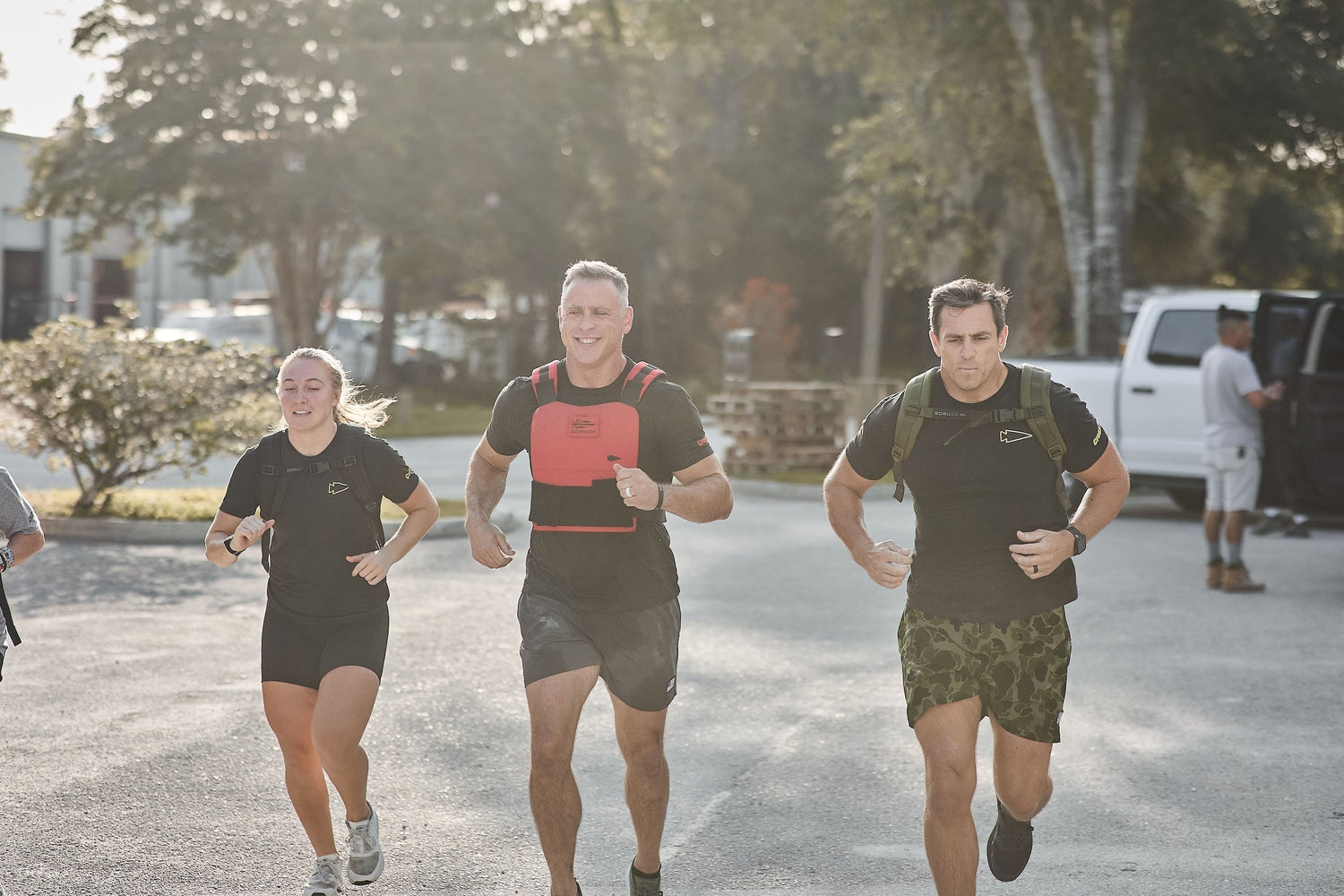 Three people rucking outdoors in GORUCK gear and weighted backpacks on a sunny day.