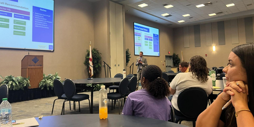 People attending a presentation in a conference room with slides displayed on two large screens
