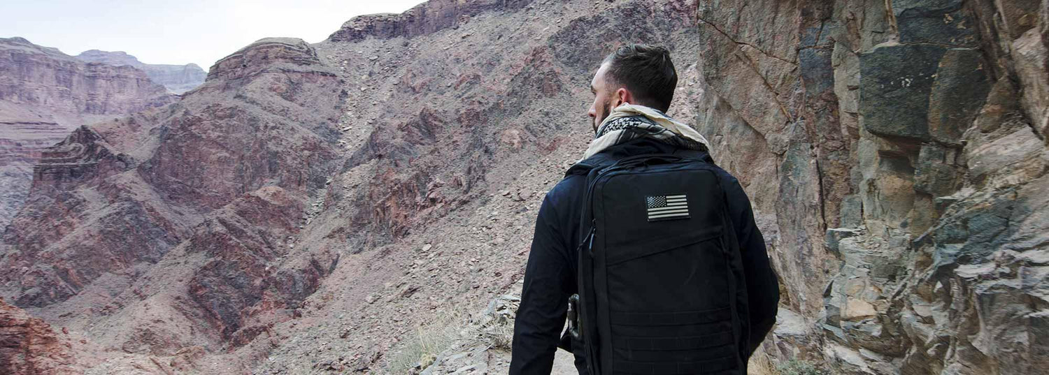Man hiking in rocky canyon wearing GORUCK backpack with American flag patch