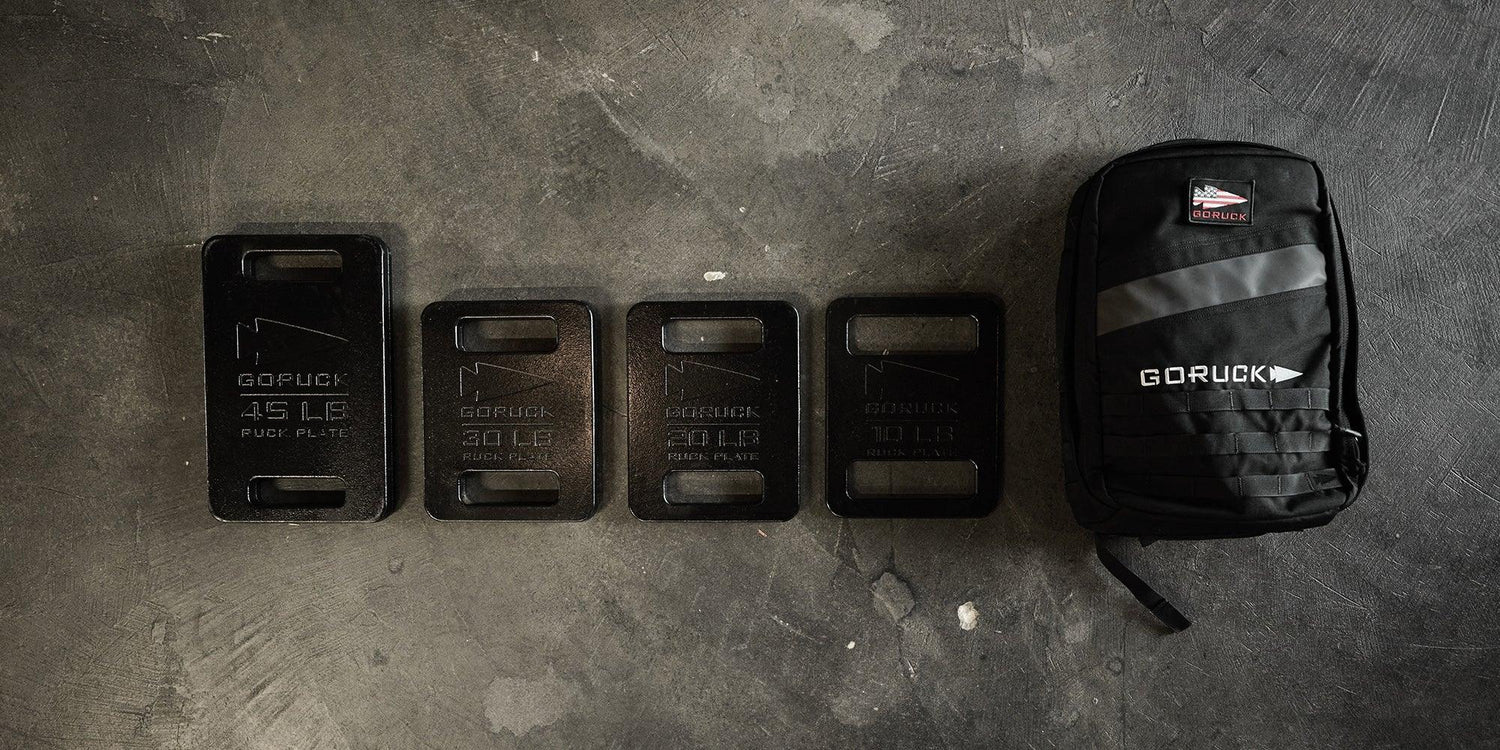 GORUCK ruck plates in various weights lined up next to a black GORUCK backpack on concrete