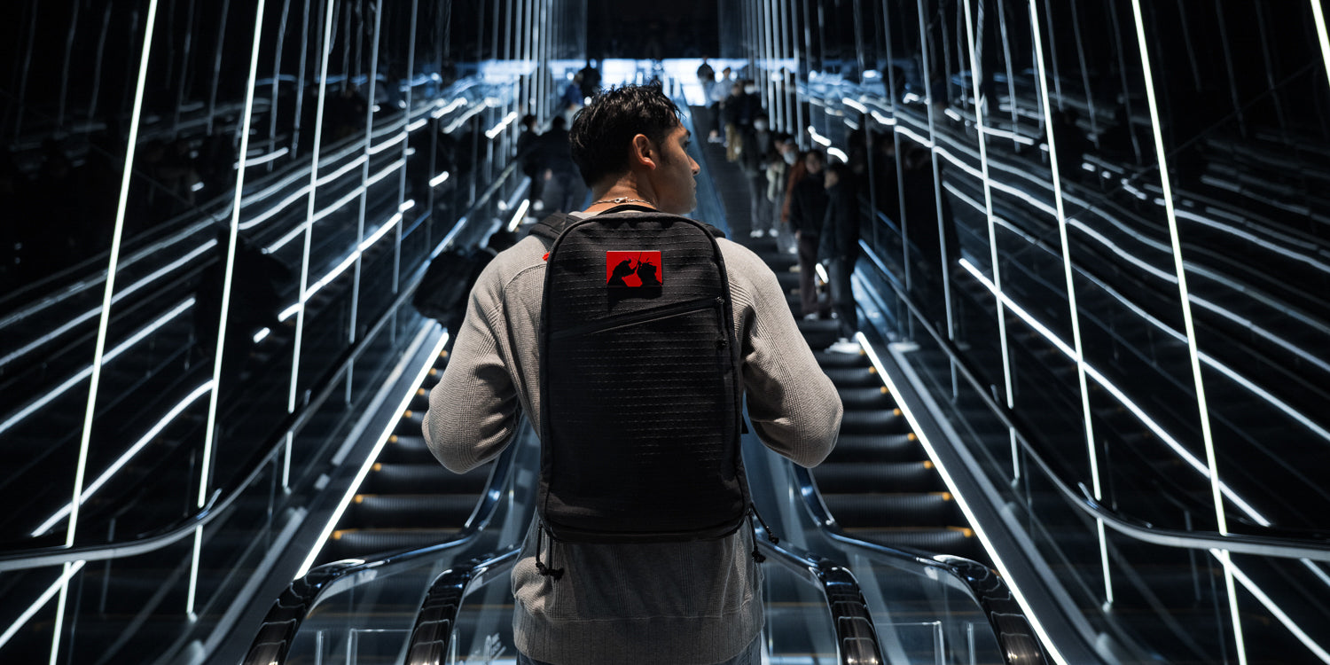 Man with a black backpack rides an illuminated escalator in a modern, futuristic building.