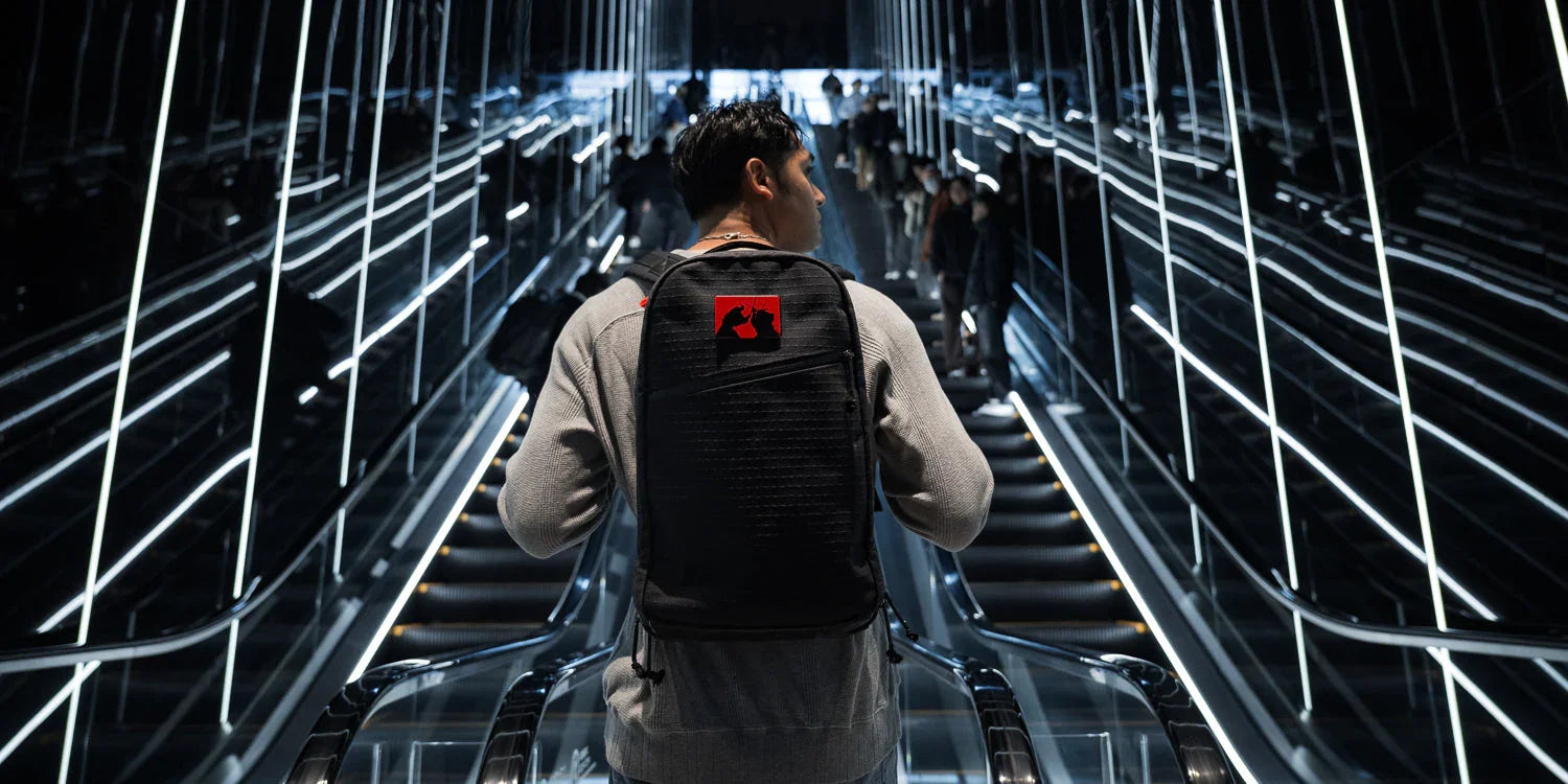 Man with a black GORUCK backpack featuring red patch on modern illuminated escalator