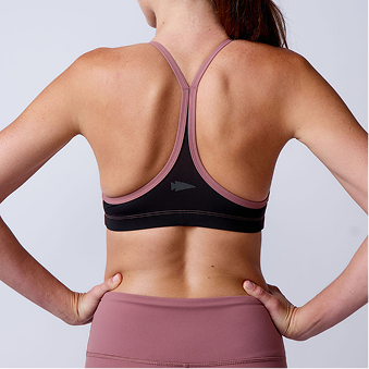 Back view of a woman wearing a mauve and black racerback sports bra and mauve leggings against a plain background