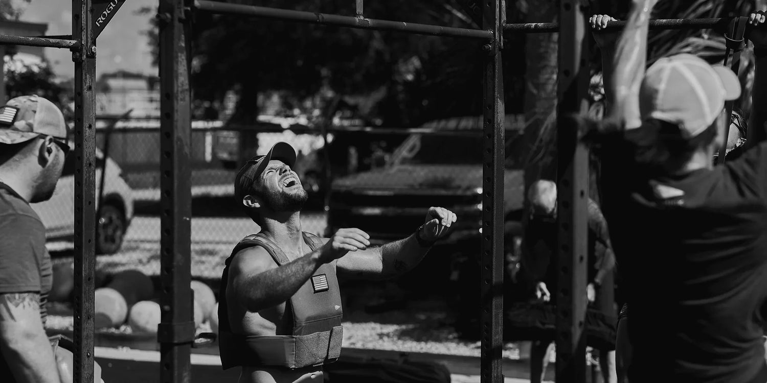 Man wearing GORUCK weighted vest stretching outdoors near pull-up bars during rucking workout