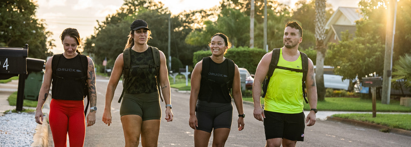 Four fit adults walking outdoors in athletic gear and GORUCK backpacks during sunset in a suburban neighborhood