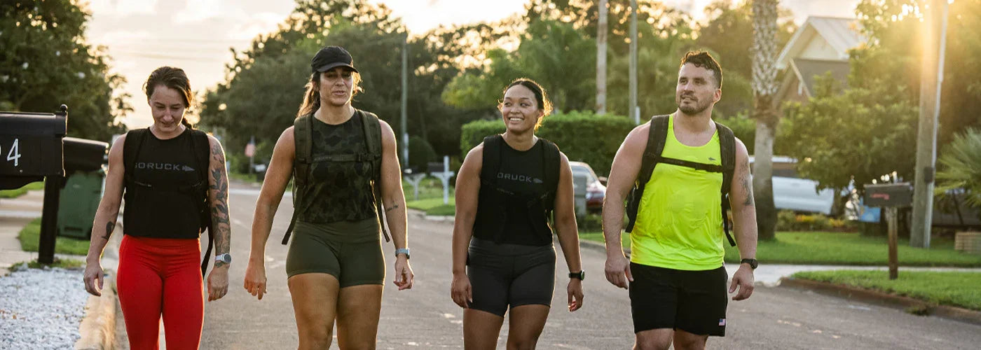 Four people wearing GORUCK gear rucking outdoors on a suburban street at sunset.