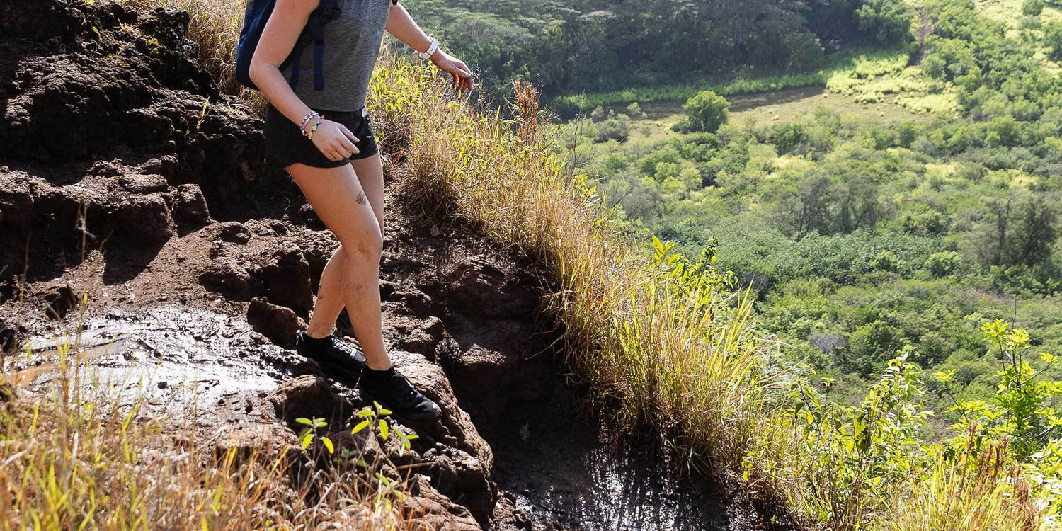 Person hiking along a steep, rocky trail with lush green valley visible in the background.