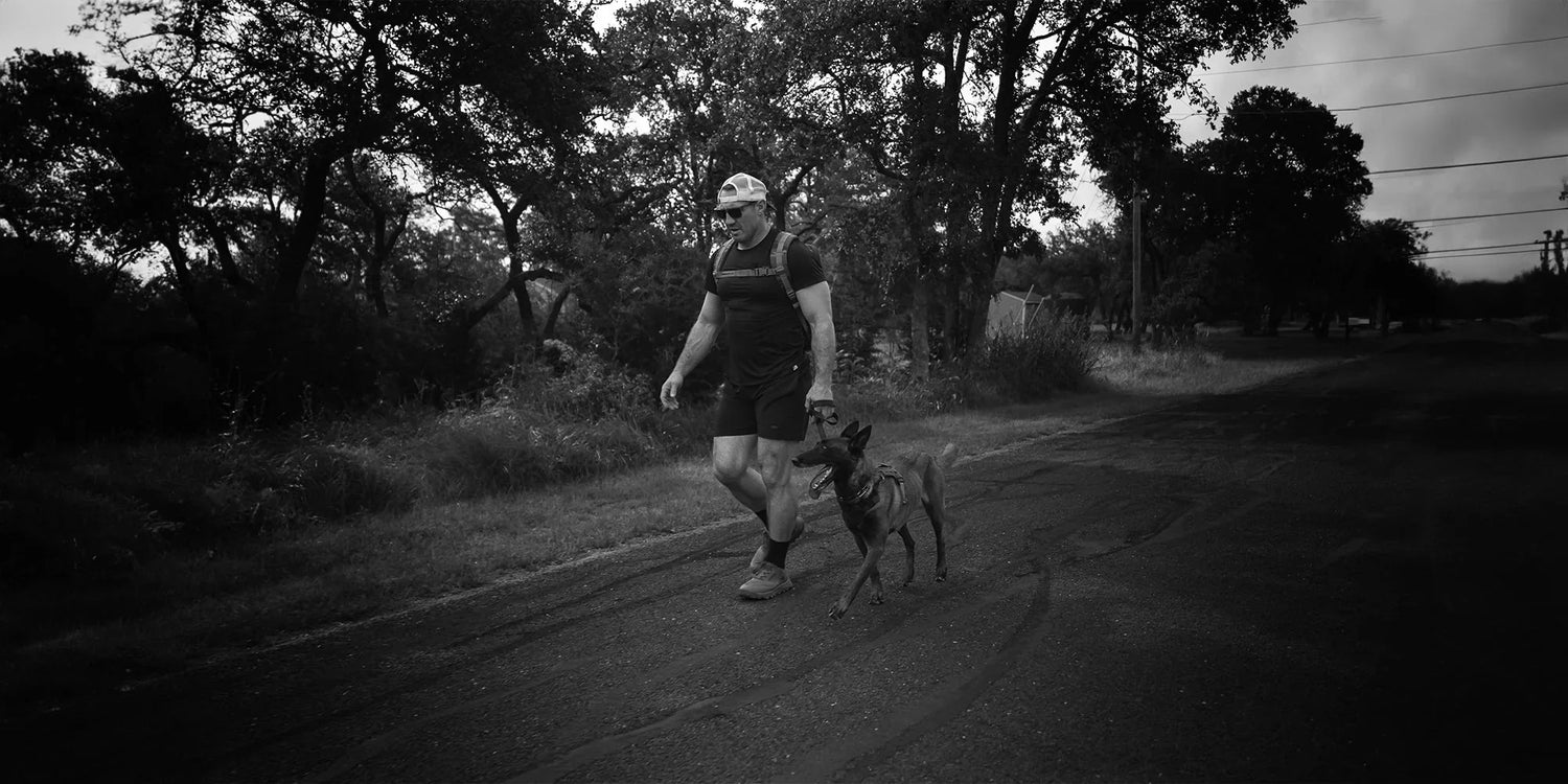 Man in GORUCK gear and footwear rucking outdoors with dog on a rural road at dusk