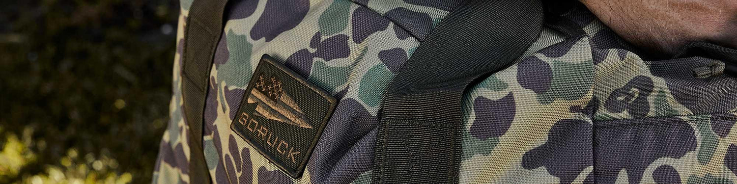 Close-up of GORUCK frogskin camo rucksack with rugged straps and patch in outdoor setting