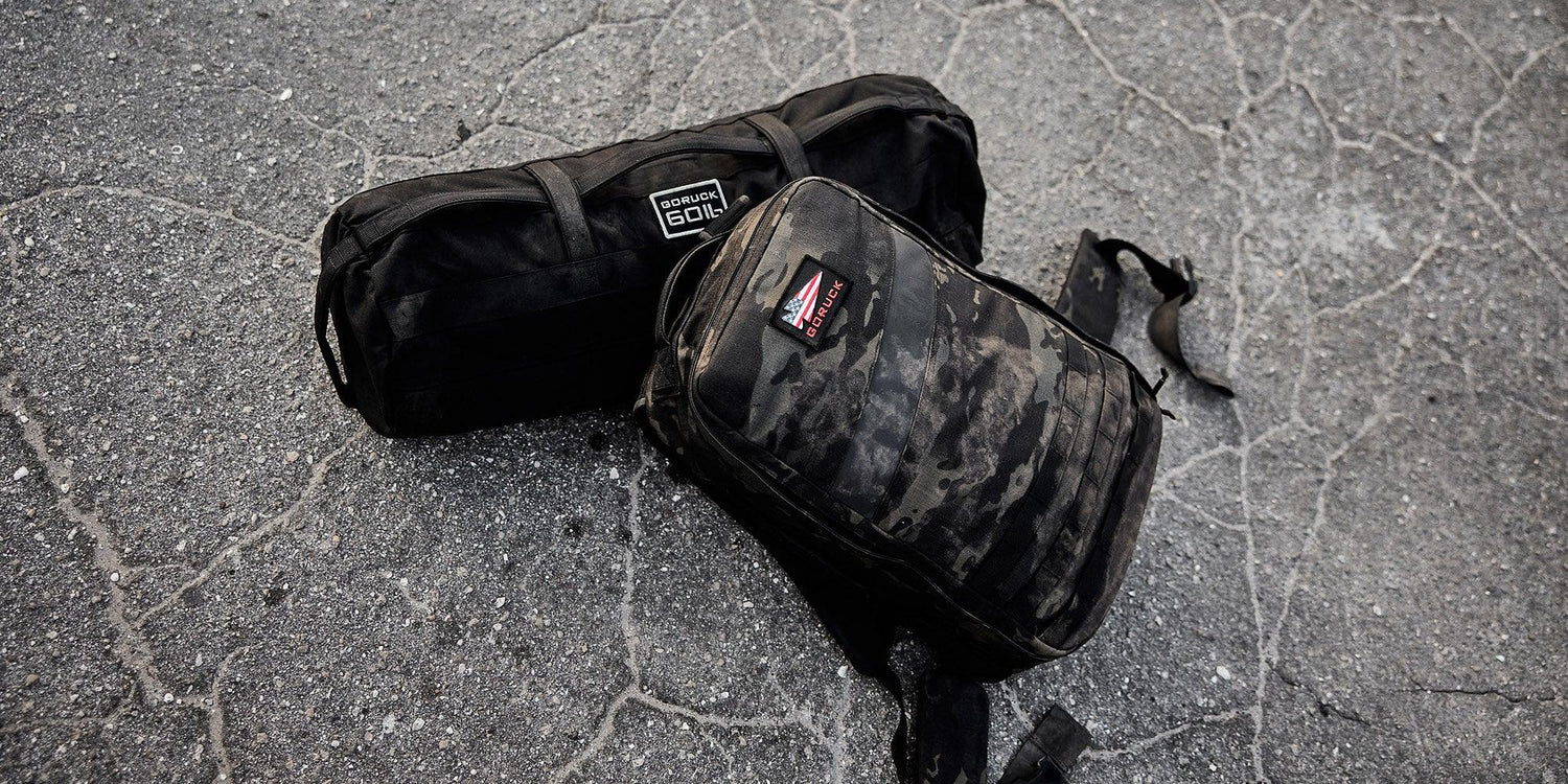 GORUCK rucksack and black gear bag on cracked asphalt, tough outdoor rucking equipment